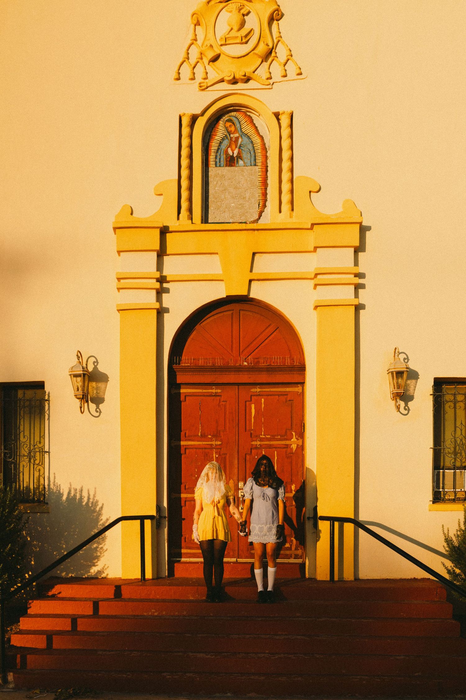 Two people standing in front of a yellow Spanish colonial church entrance at sunset.