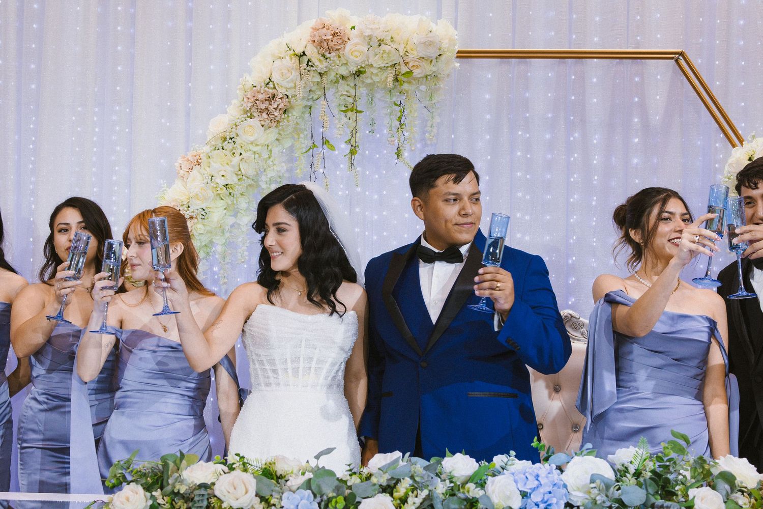 Wedding party in lavender dresses toasting with champagne glasses at an elegant reception.