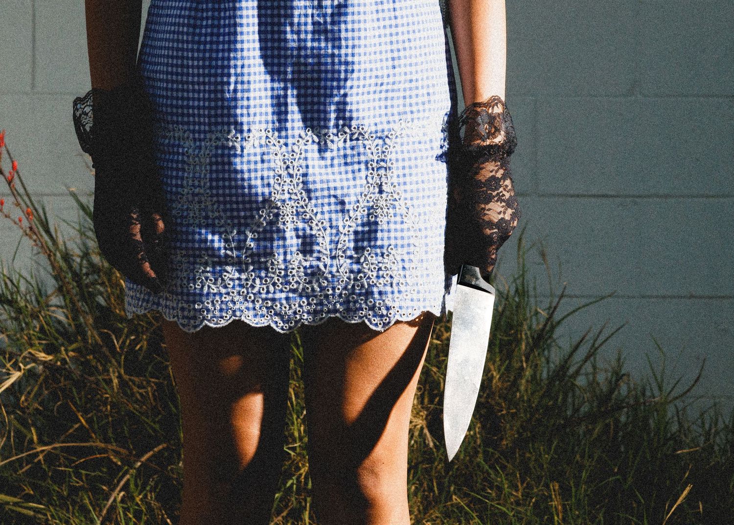 Close-up details of a blue gingham dress with white lace trim against a wall.