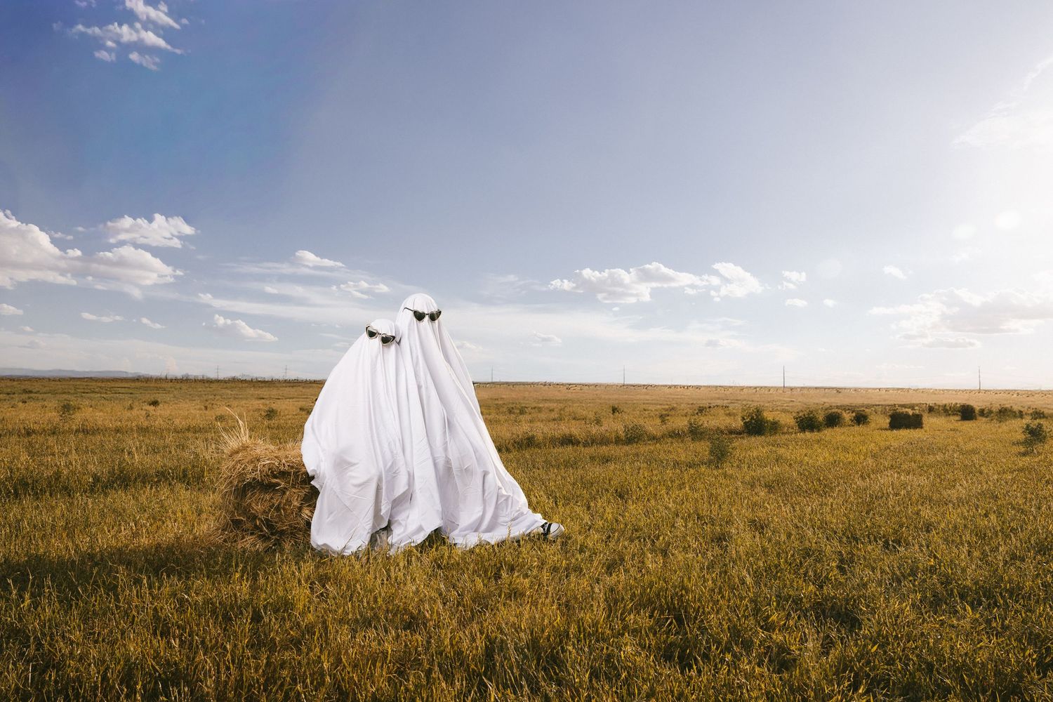 White-sheeted figures stand mysteriously in a vast grassy landscape at sunset.