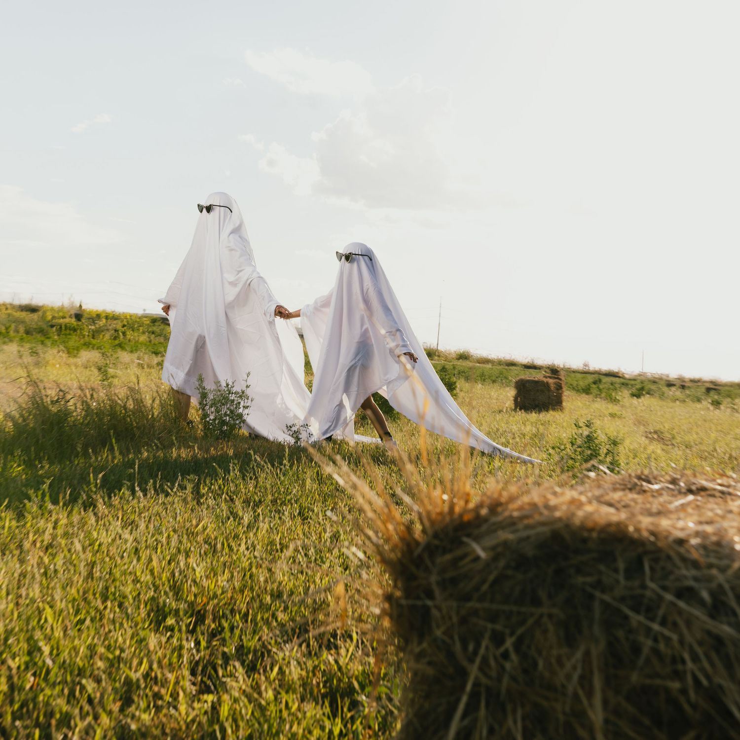 Ghost-like figures in white sheets stand in a golden field during sunset.
