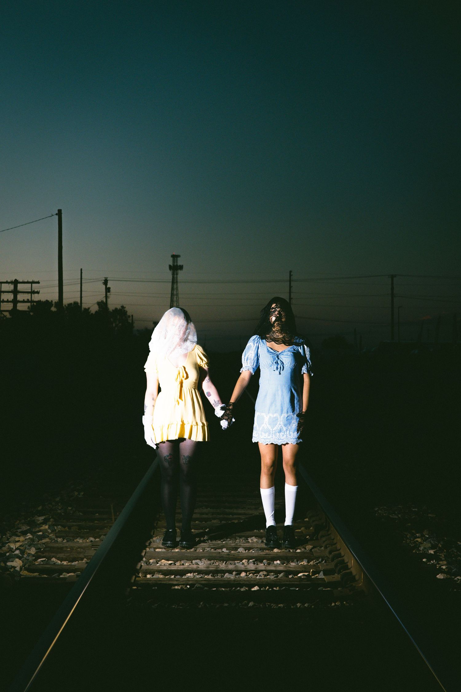 Silhouettes of people in dresses standing on train tracks at dusk.
