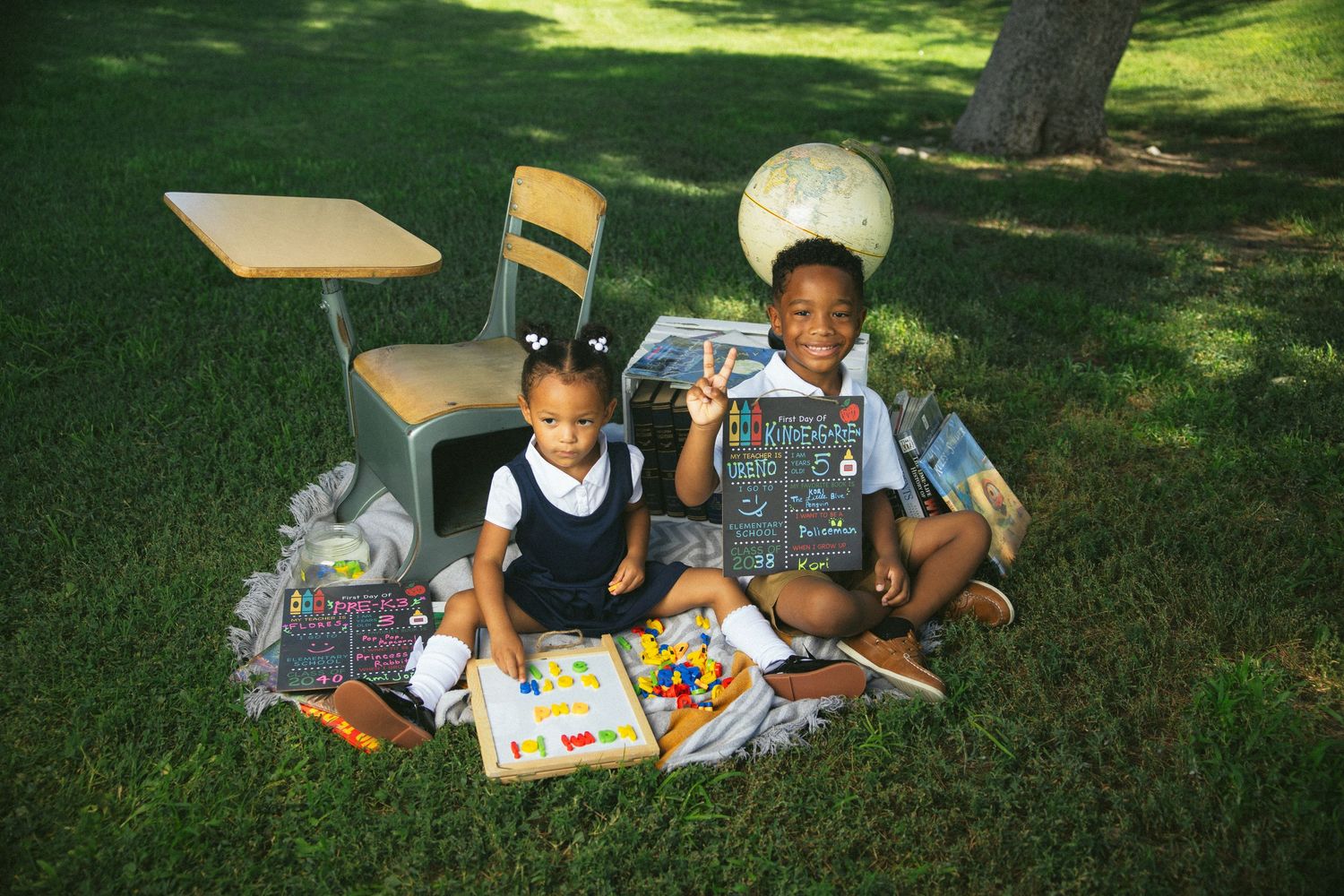 Two students study together outdoors on grass with a desk and school supplies on a sunny day.