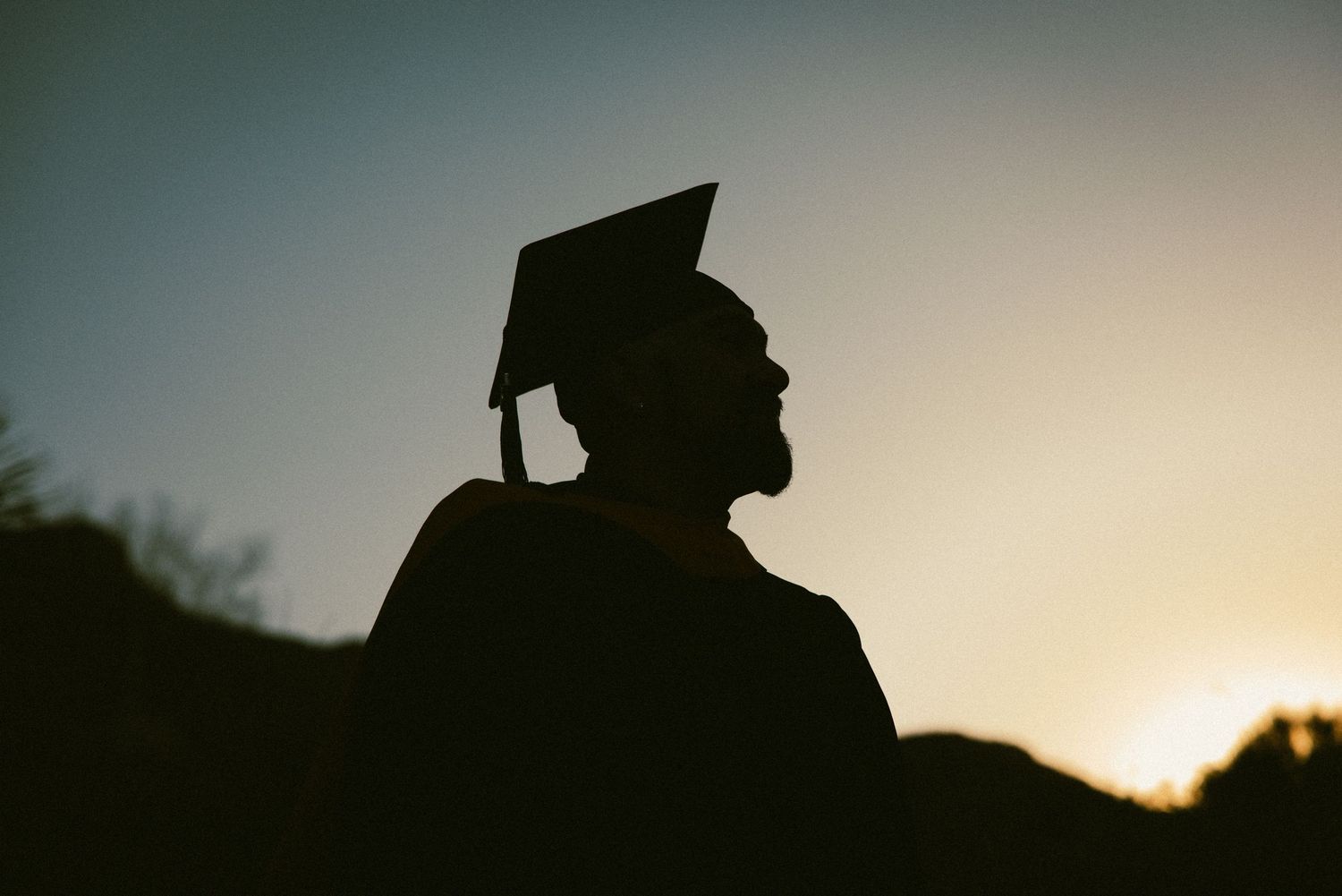 Silhouette of graduation cap being tossed against sunset sky.
