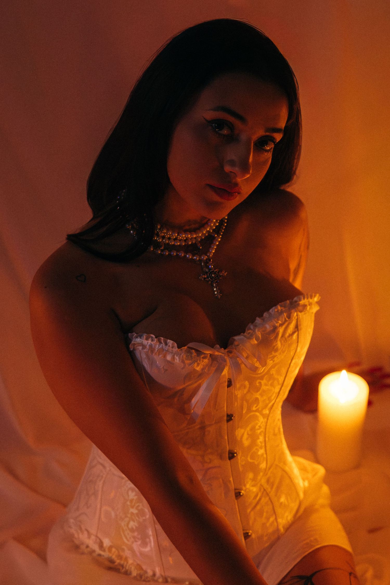 Dramatic portrait with candlelight featuring white lace corset and pearl choker.