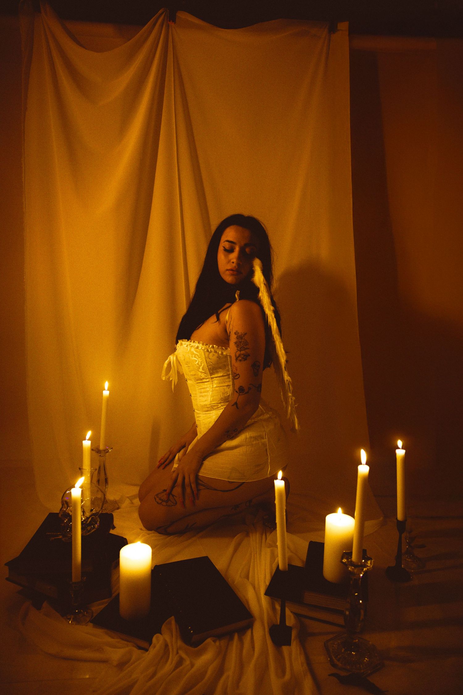 Ethereal candlelit scene with white corset against draped fabric backdrop.