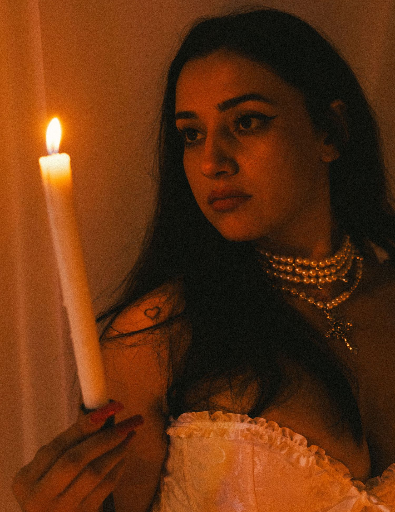Romantic portrait illuminated by single candle featuring pearl necklace and white corset.