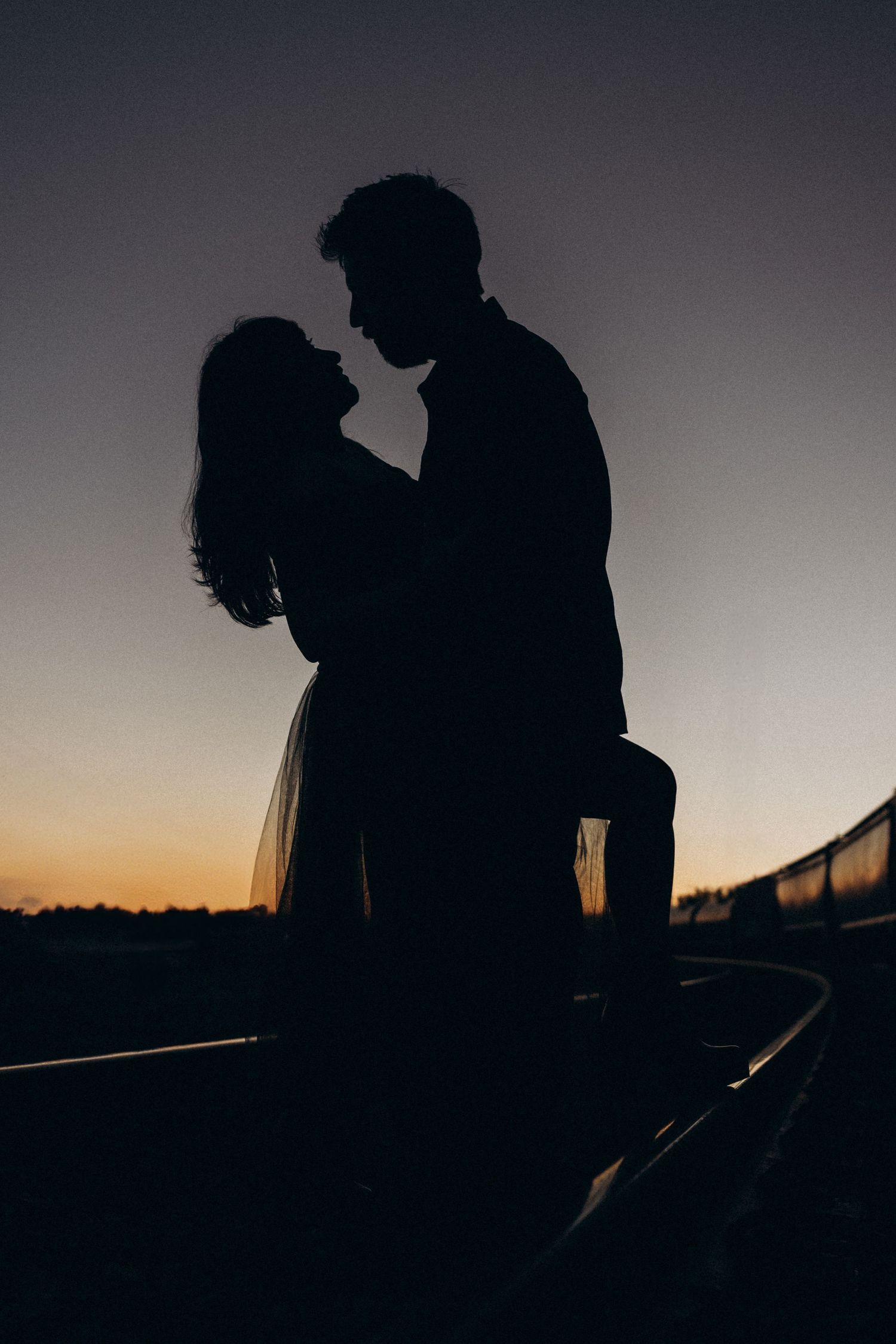Romantic silhouette of couple embracing against sunset sky.