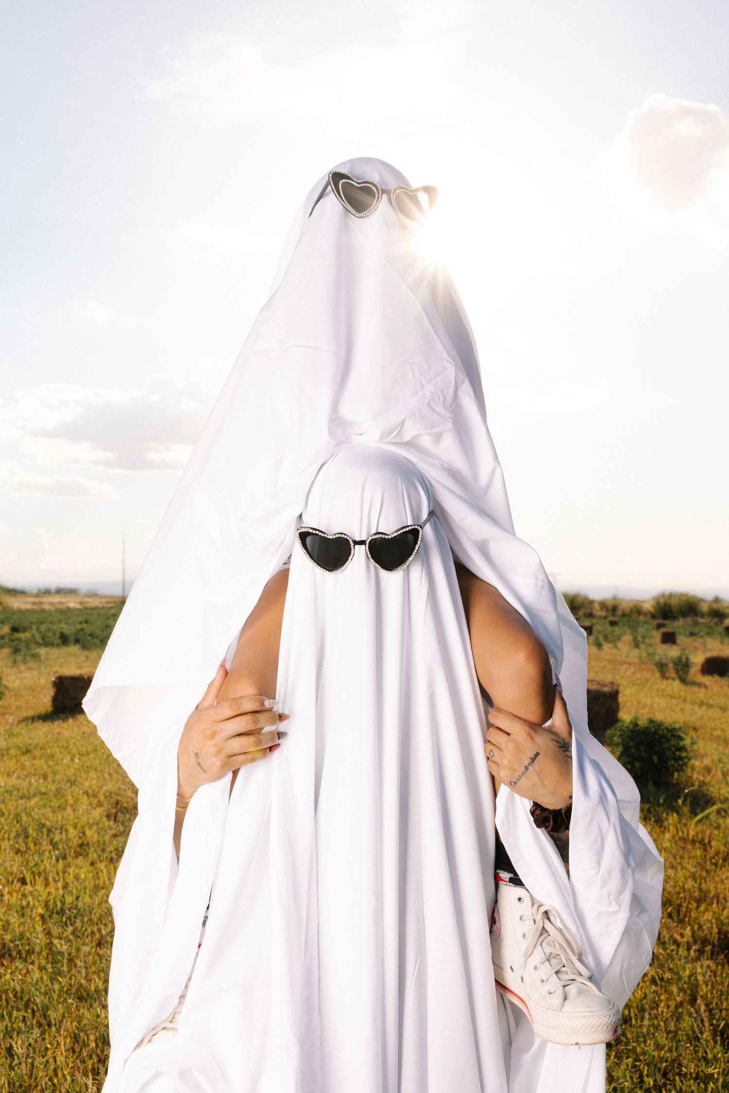 Two figures in white ghost costumes pose playfully in a sunny field.
