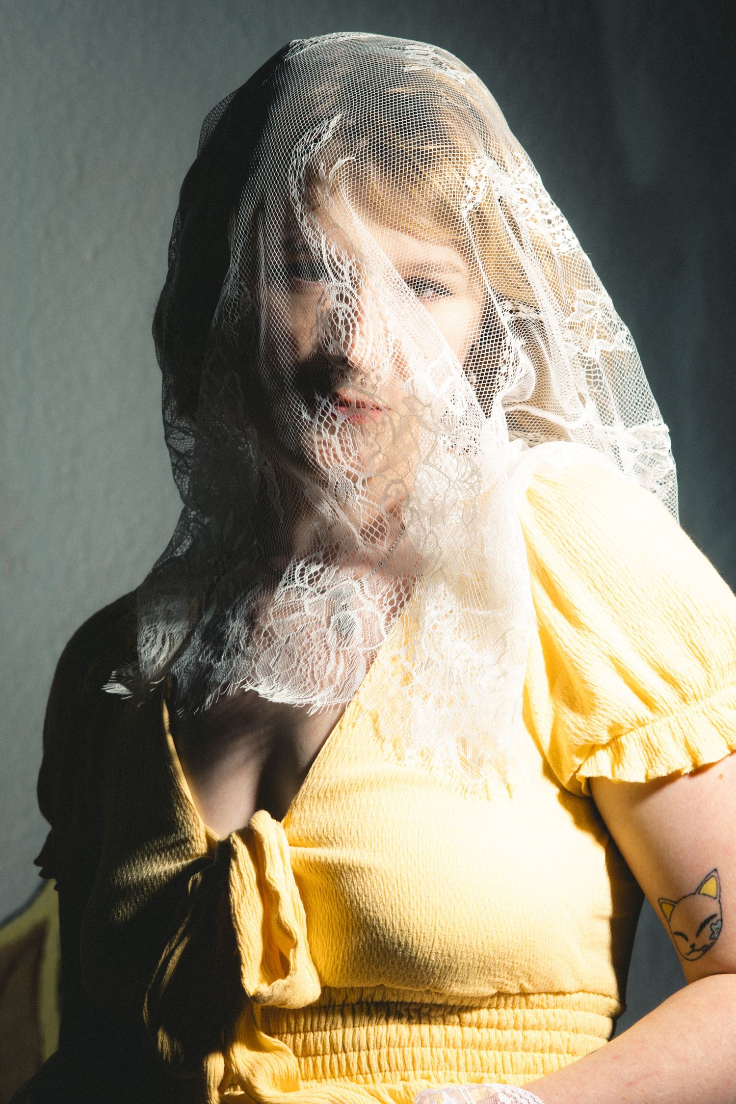 Figure wearing a yellow dress with translucent fabric draped over them in dramatic lighting.