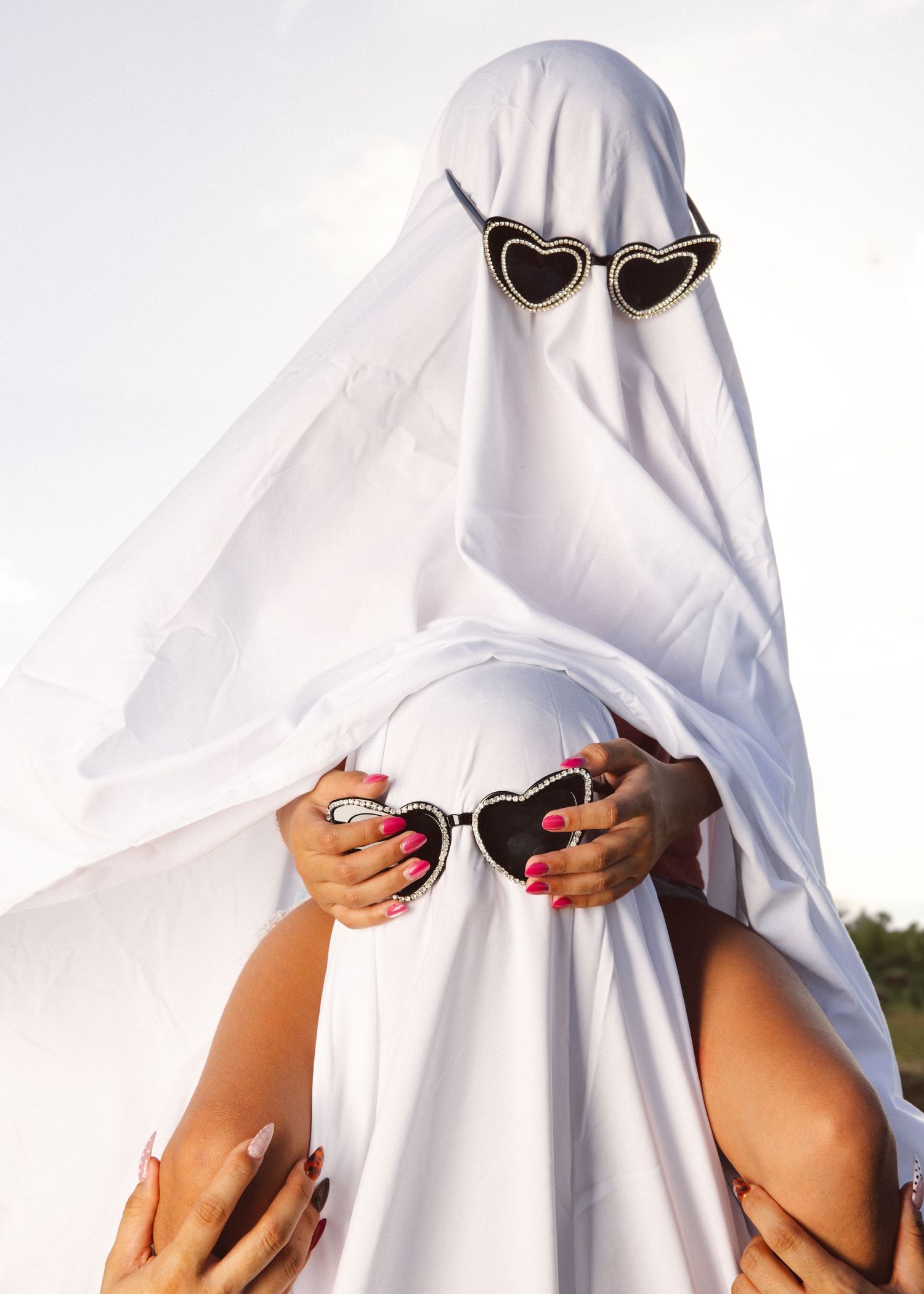 Figures in ghost costumes wearing sunglasses pose in white sheets against bright background.