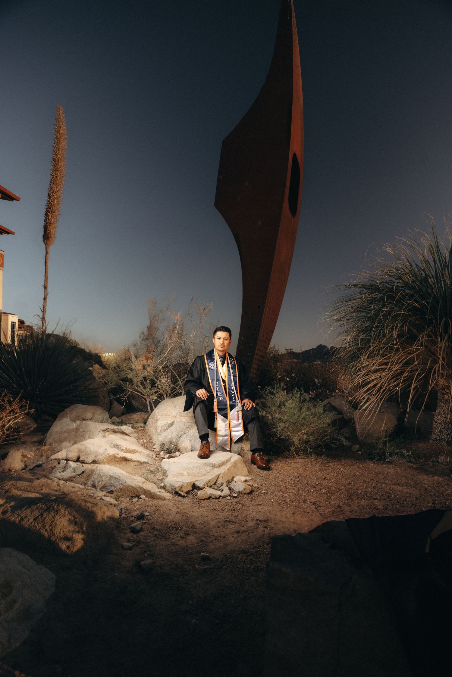 Desert landscape scene with artistic metal sculptures and natural rock formations at sunset.