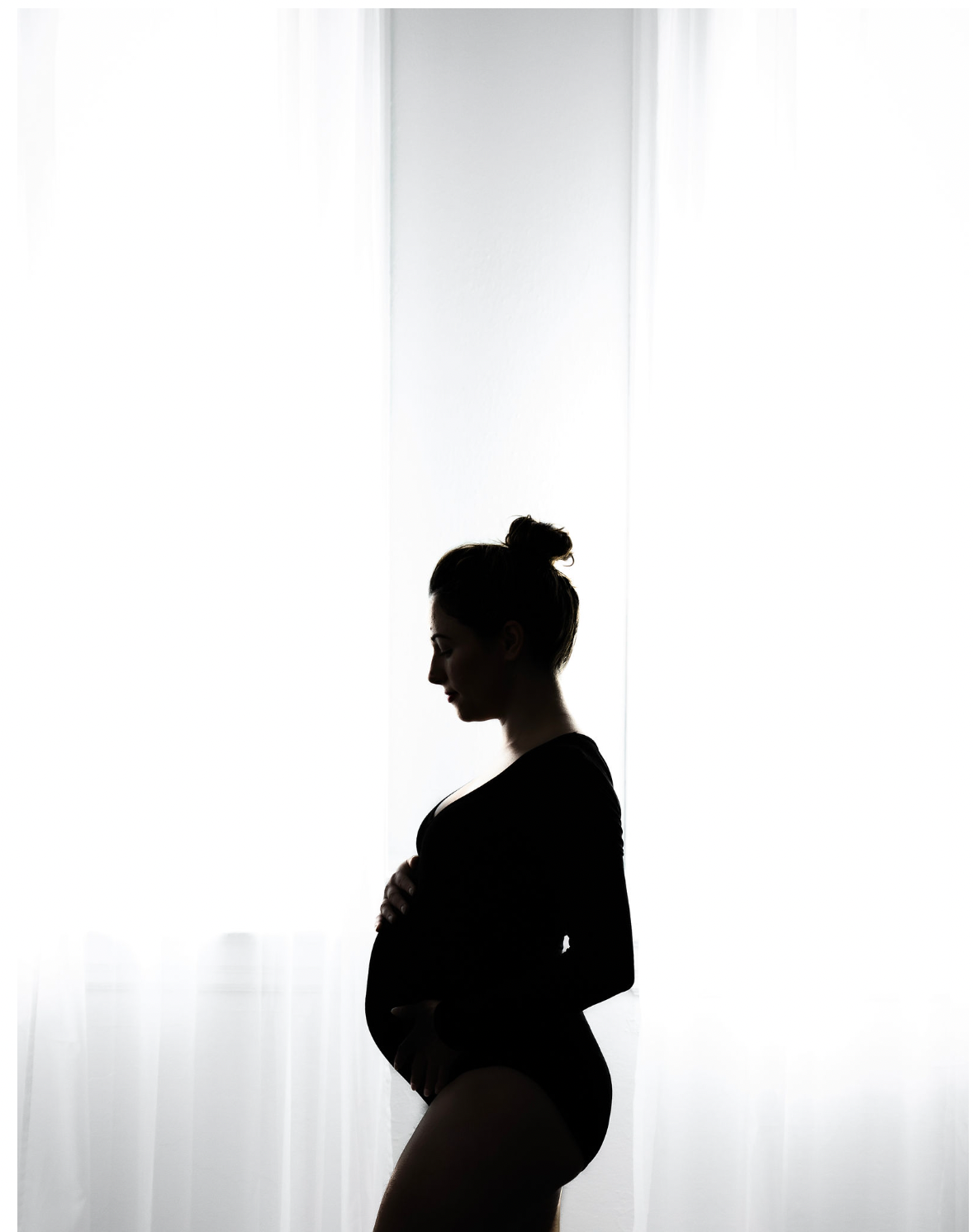 Silhouette of a pregnant woman in profile against a white background with soft lighting.