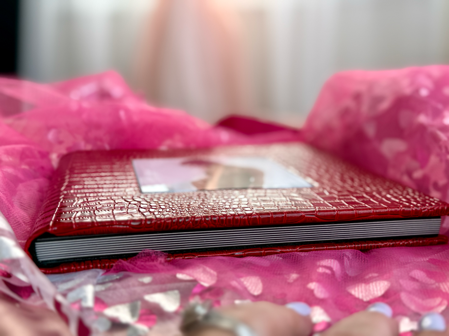 A textured red leather notebook rests on pink fabric with a soft blurred background.
