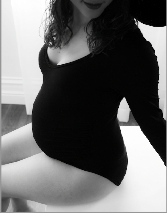 A black and white photo shows a person wearing a black dress during pregnancy, captured in a candid moment.