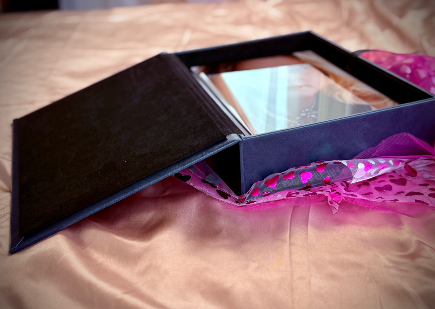 Open black gift box with mirror on pink satin fabric background.