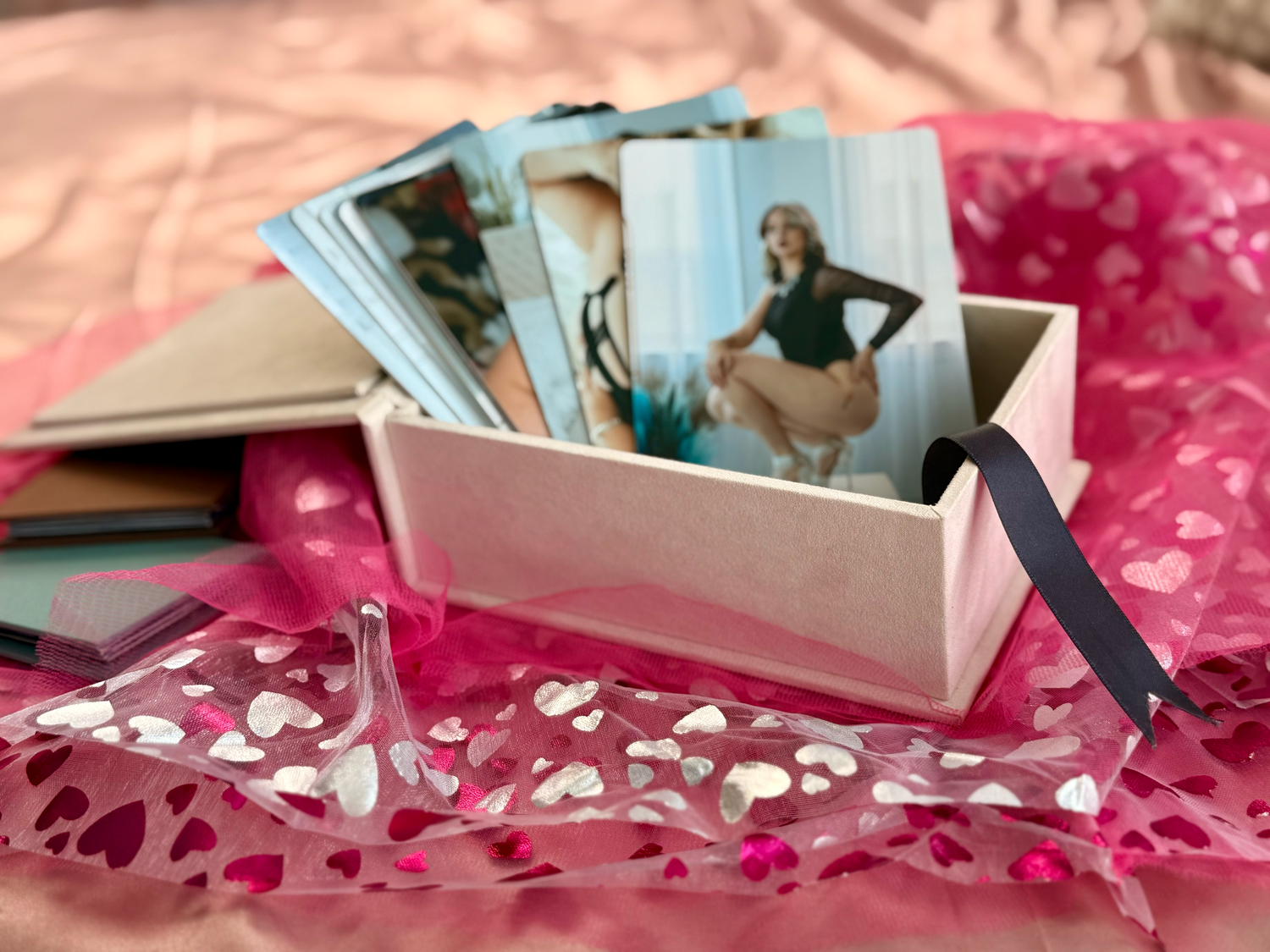 An open box of vintage photographs sits on pink fabric scattered with small metallic heart confetti.