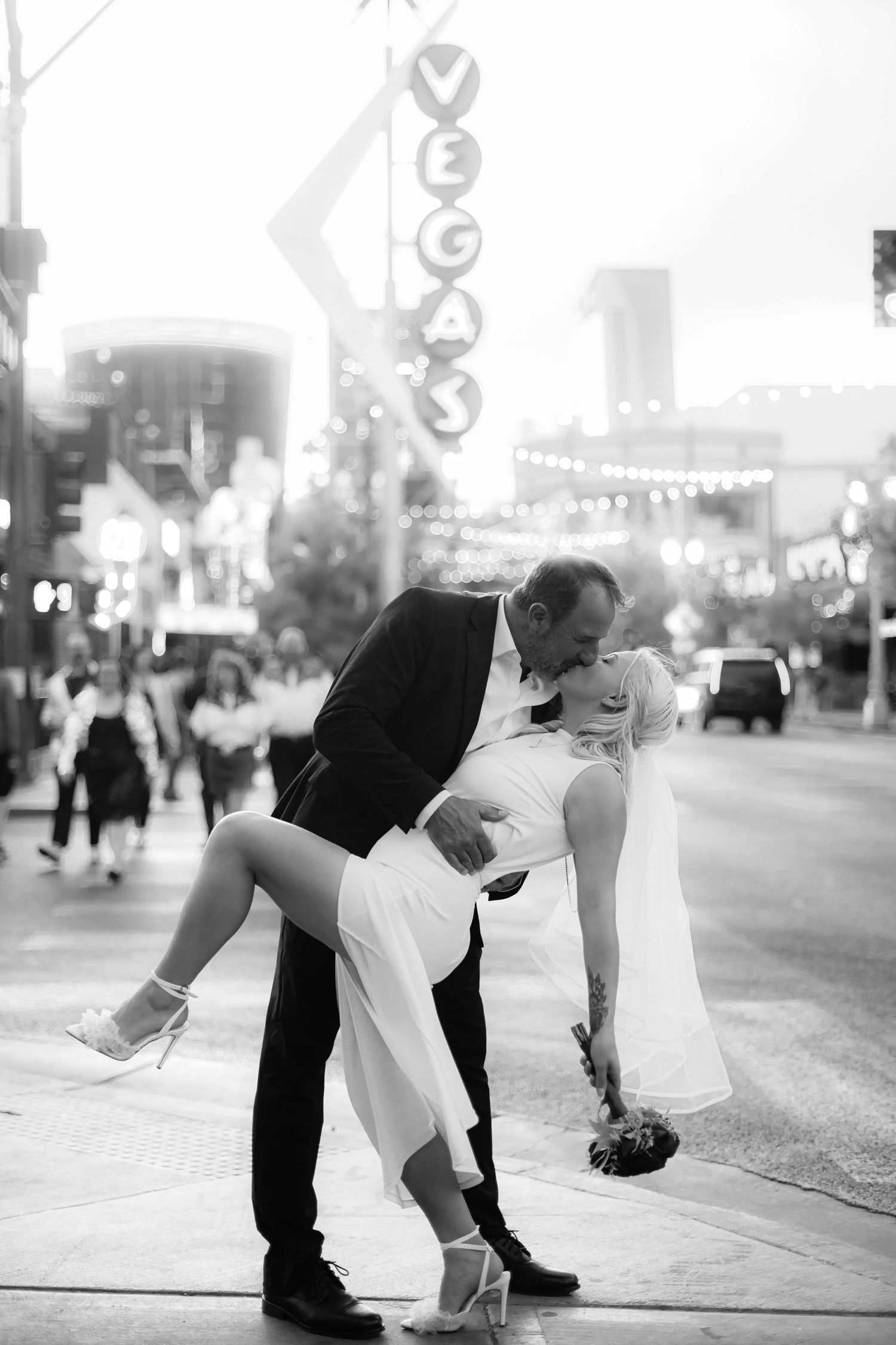 A couple shares a romantic dip kiss on a Las Vegas street at night with neon lights in the background.