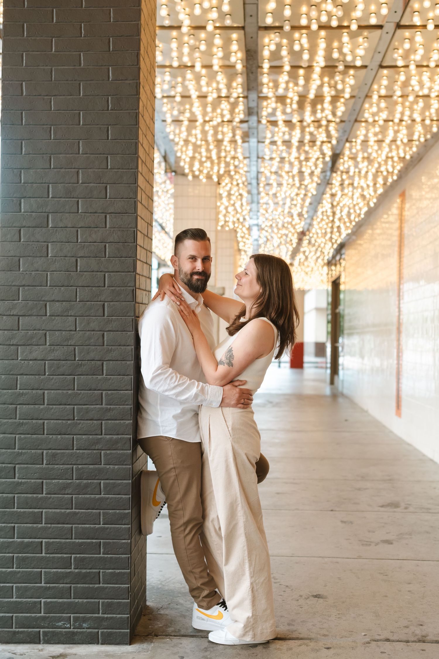 Couple shares intimate moments in an industrial hallway with sparkling overhead lights.