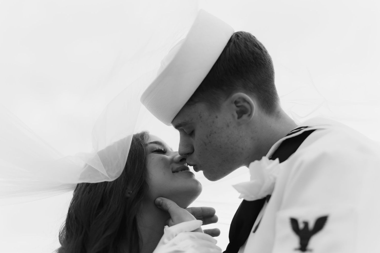 Black and white photo of a Navy sailor in uniform sharing a romantic kiss with a woman in a white veil.