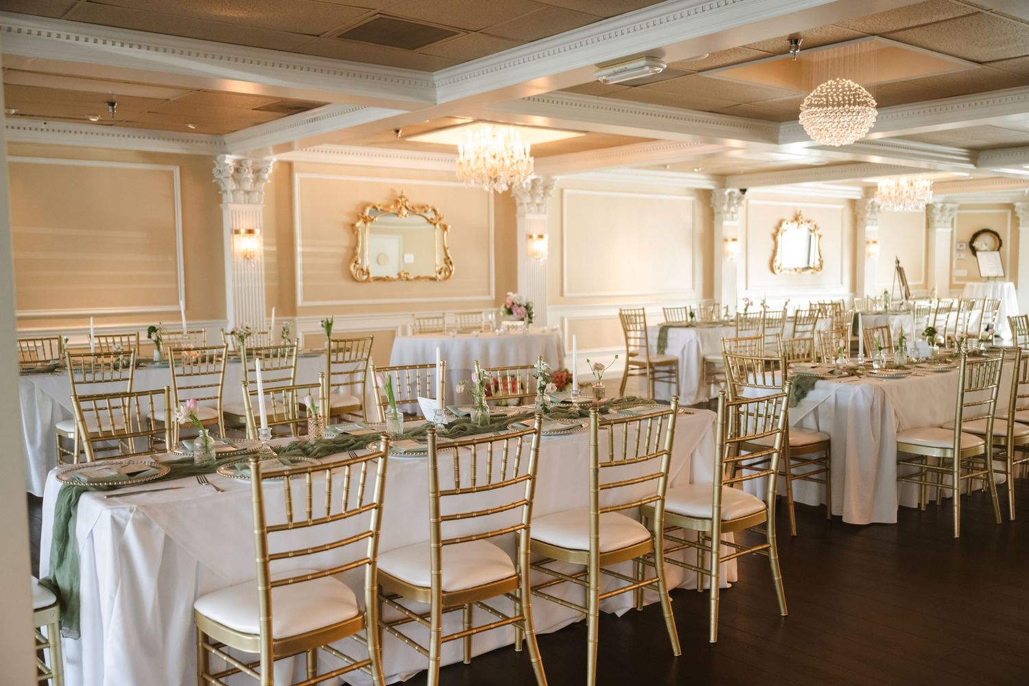 Elegant wedding reception hall with gold chiavari chairs, white linen tables, and crystal chandeliers in a classic ballroom.