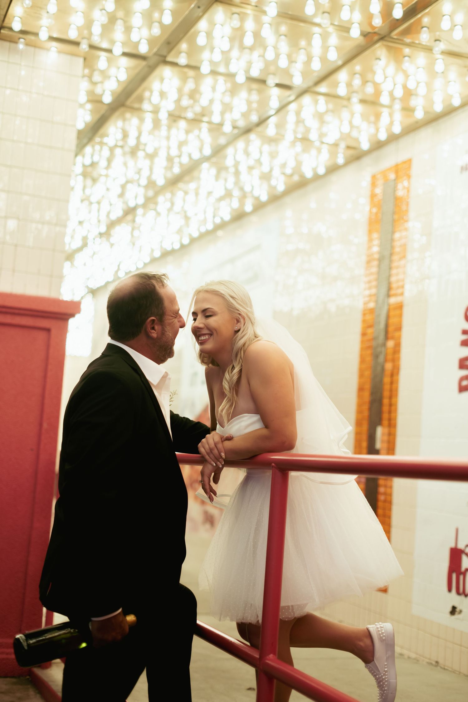 A playful wedding moment captured under twinkling lights in an industrial space.