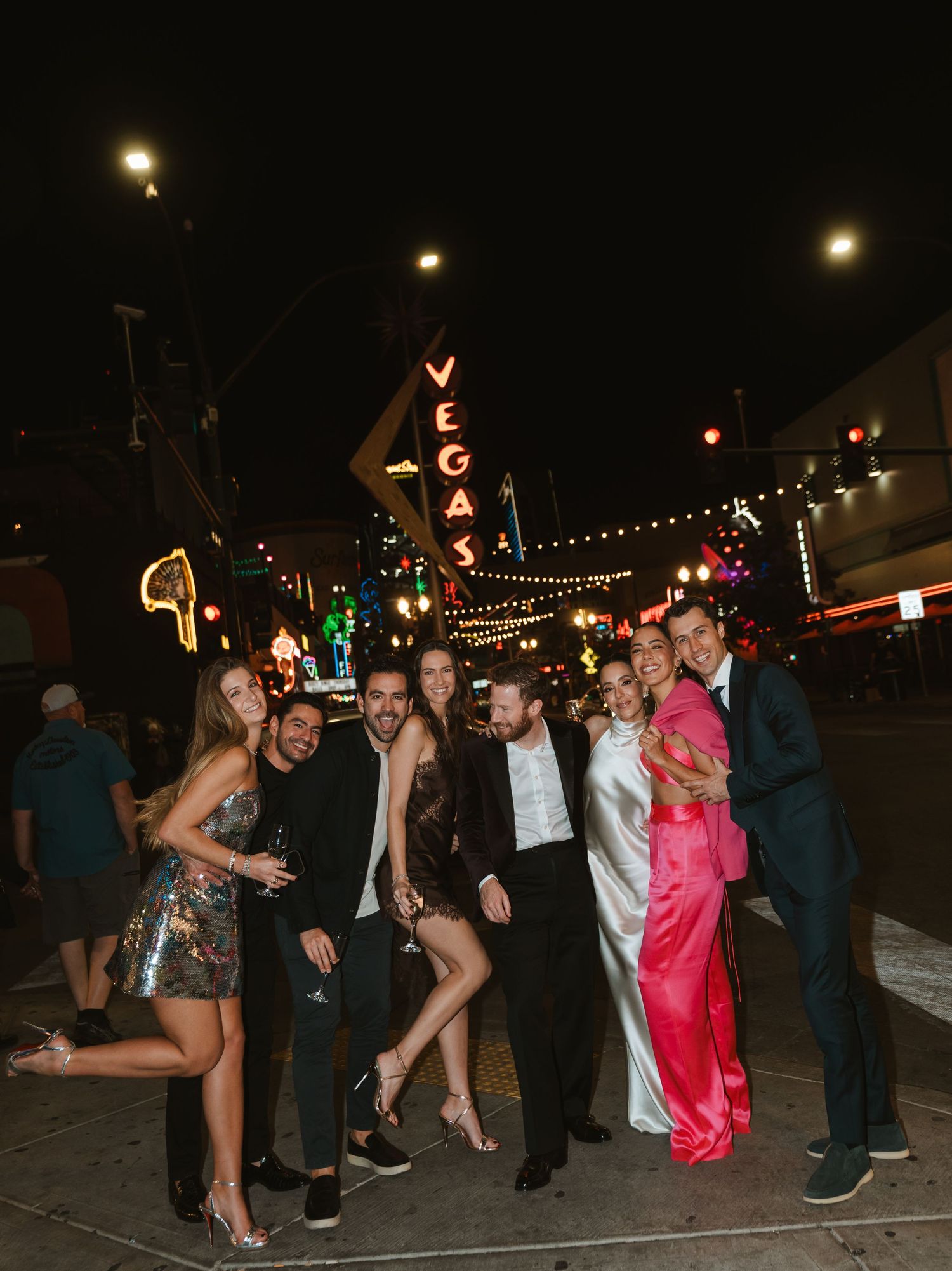 Group of friends posing on Fremont Street in Las Vegas at night, dressed in elegant party attire.