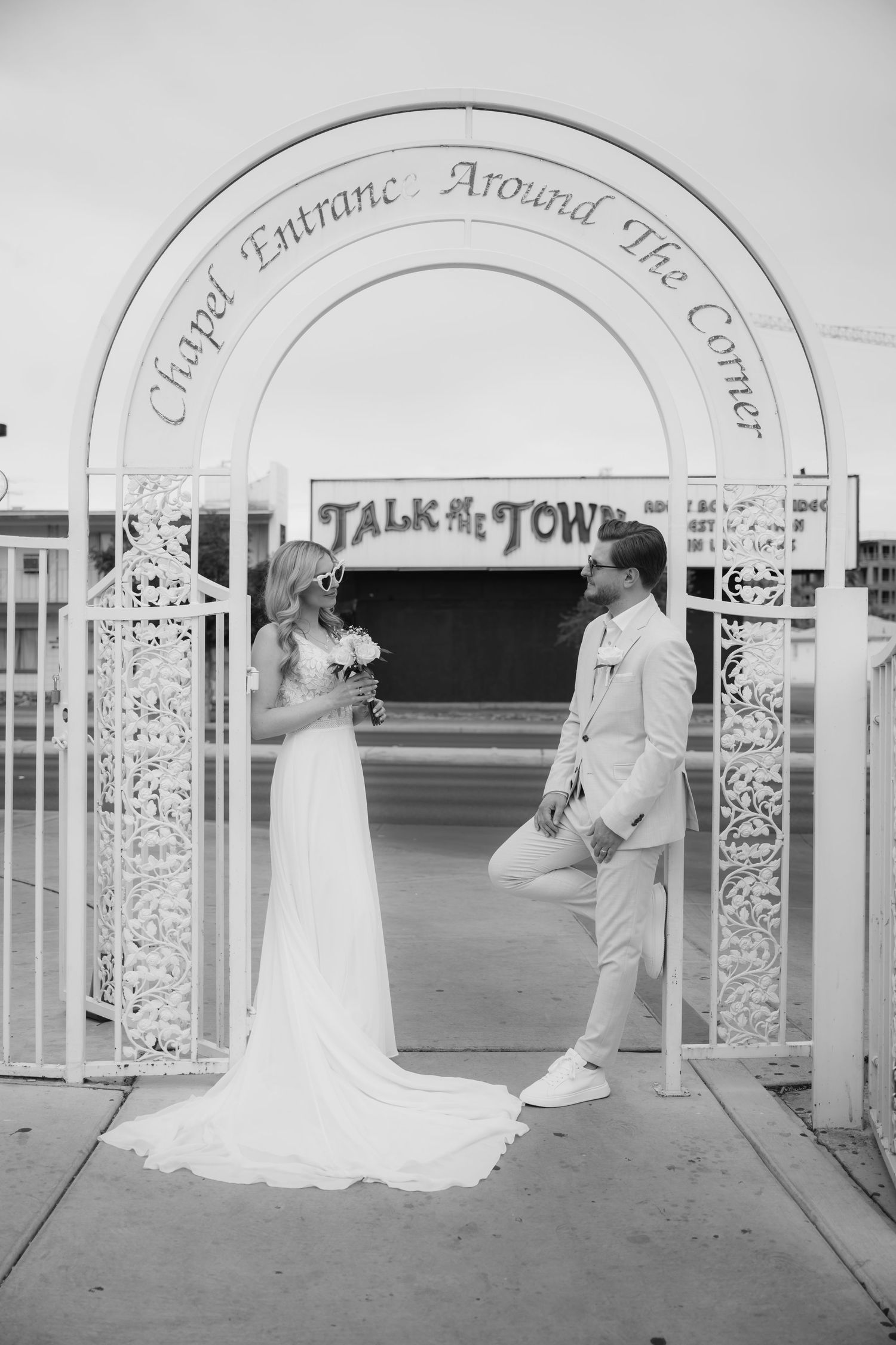 Black and white photo of a bride and groom standing under a decorative arch at Talk of the Town chapel in Las Vegas.
