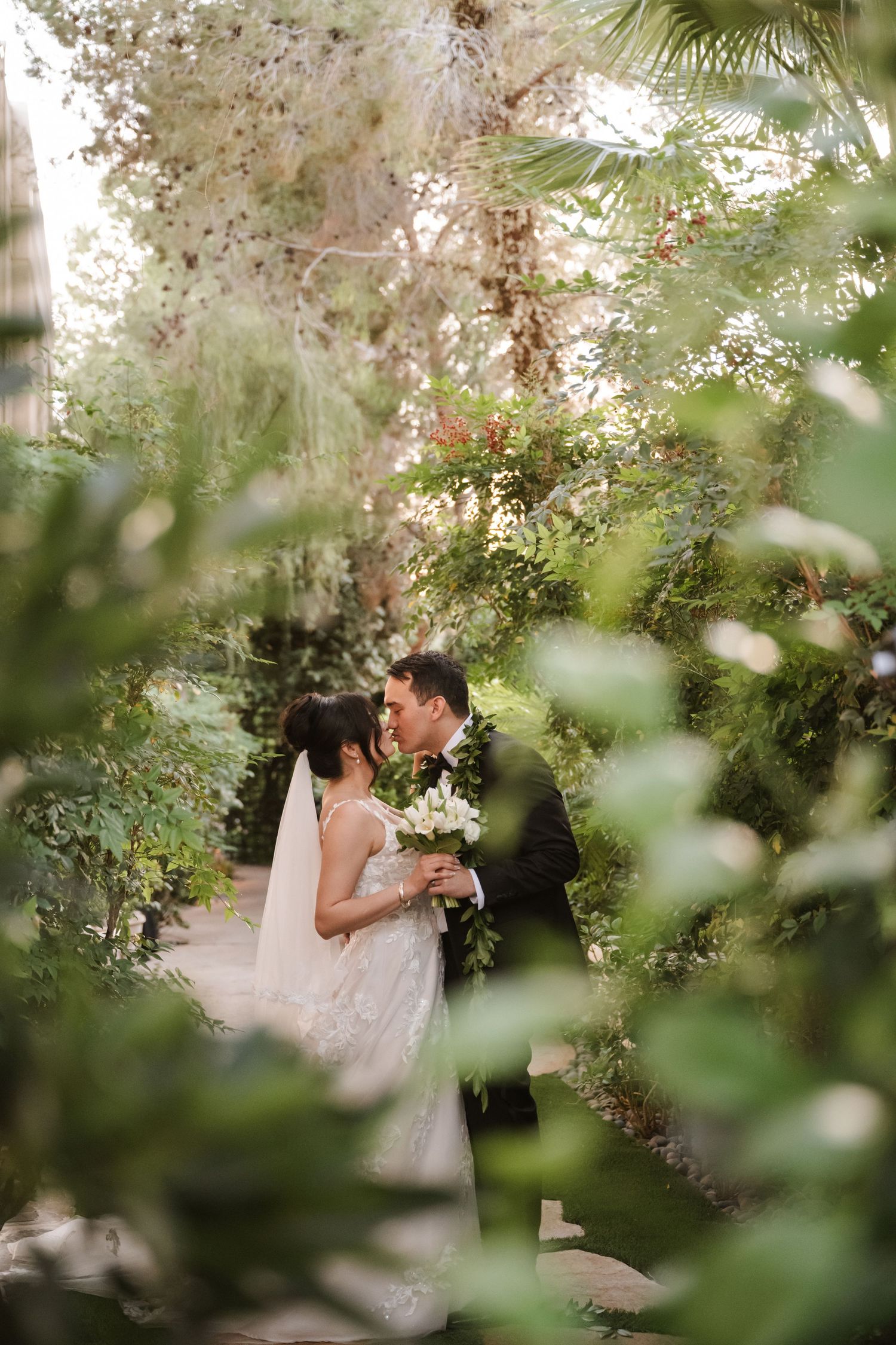 Bride and groom share a romantic kiss surrounded by lush greenery in a garden wedding setting.