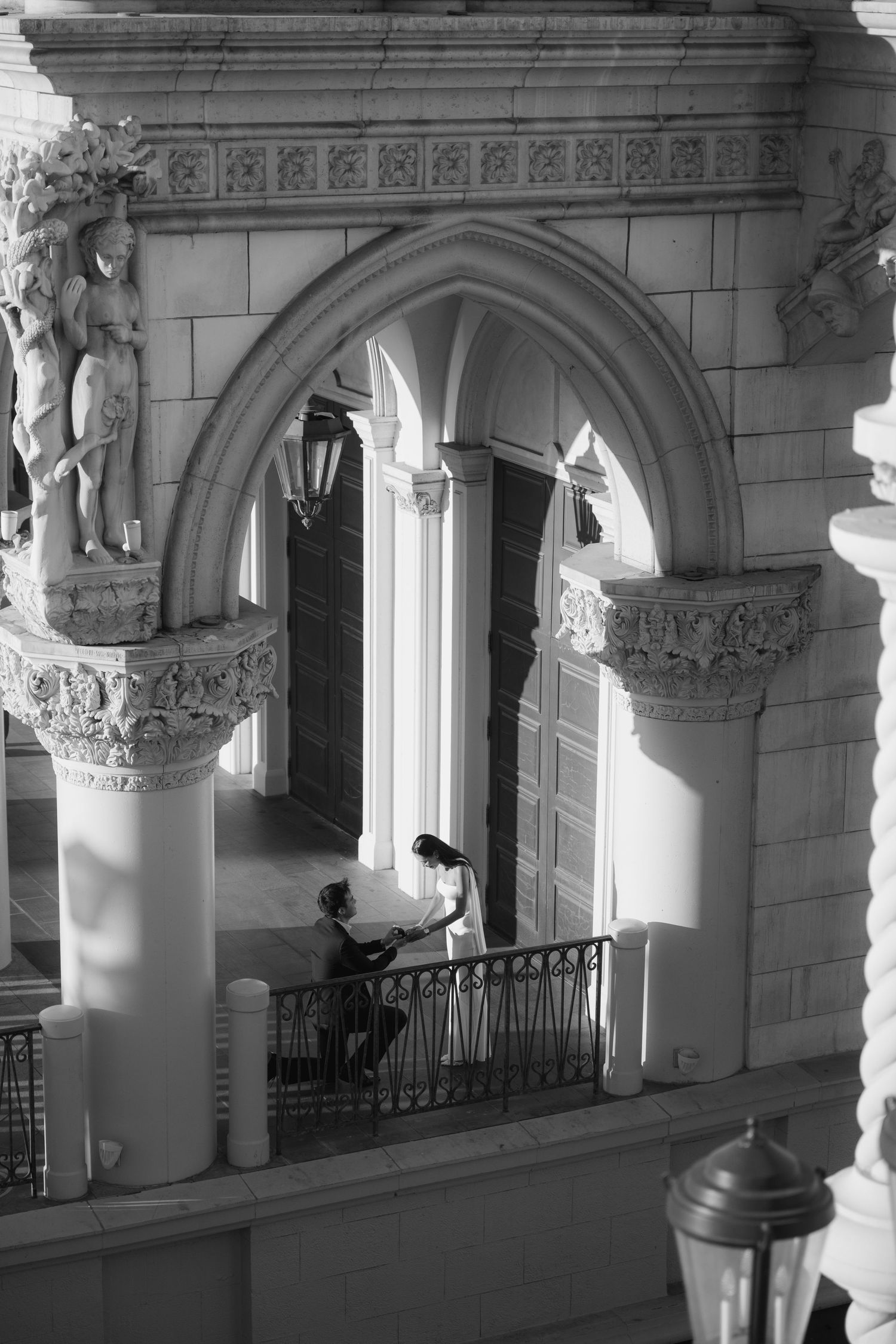 Black and white photo of a couple on an ornate balcony with Gothic arches and classical sculptures.