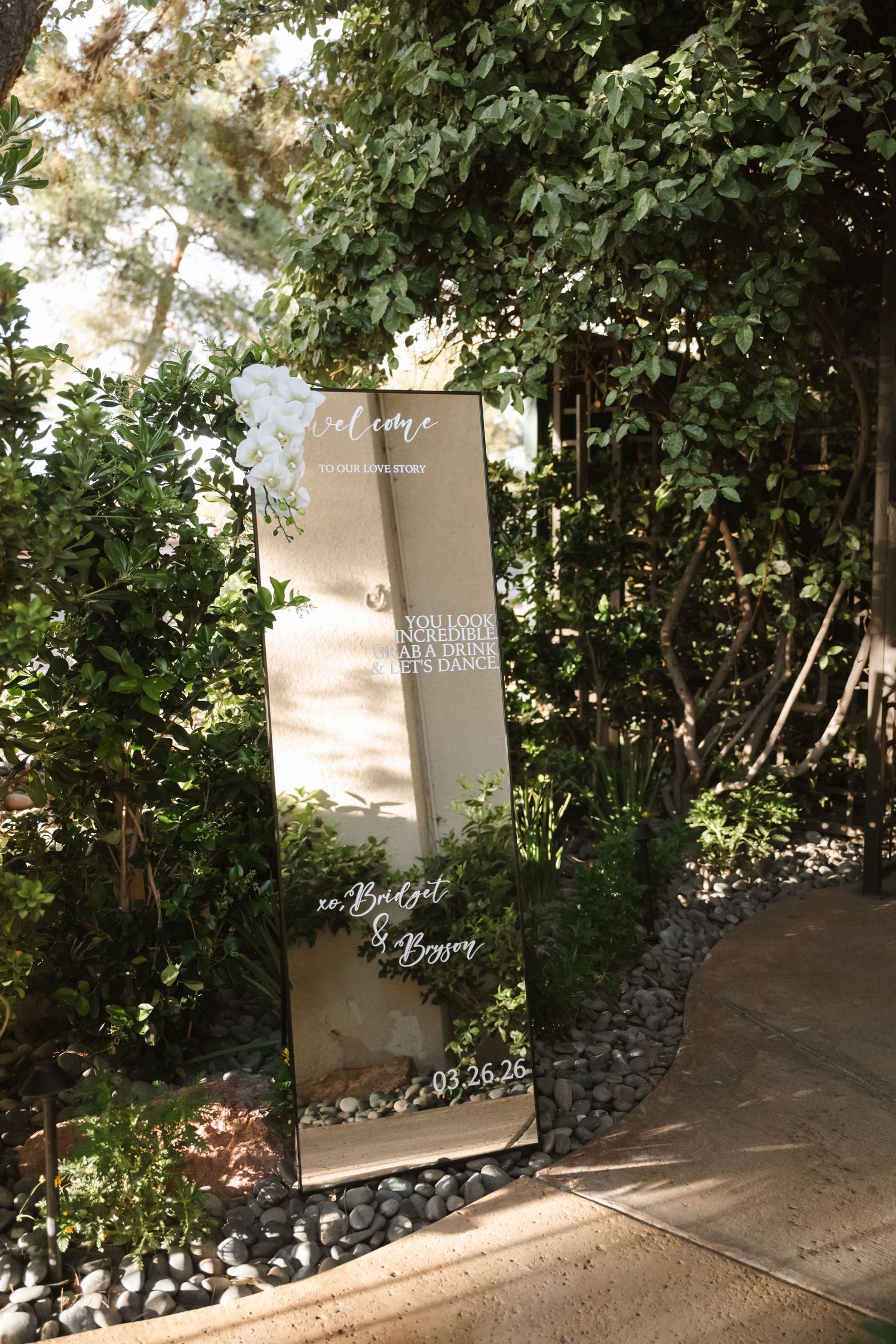 Elegant mirrored wedding welcome sign surrounded by lush greenery, personalized for Bridget and Bowen on 03.26.26.
