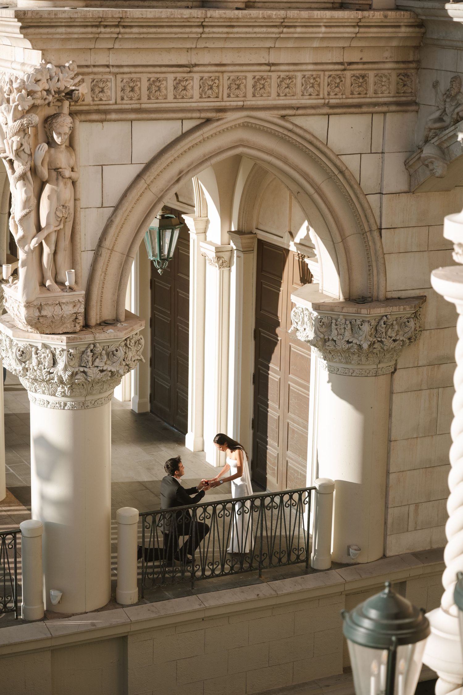 Man proposing to woman on ornate balcony with Gothic arches and classical sculptures at The Venetian Las Vegas.