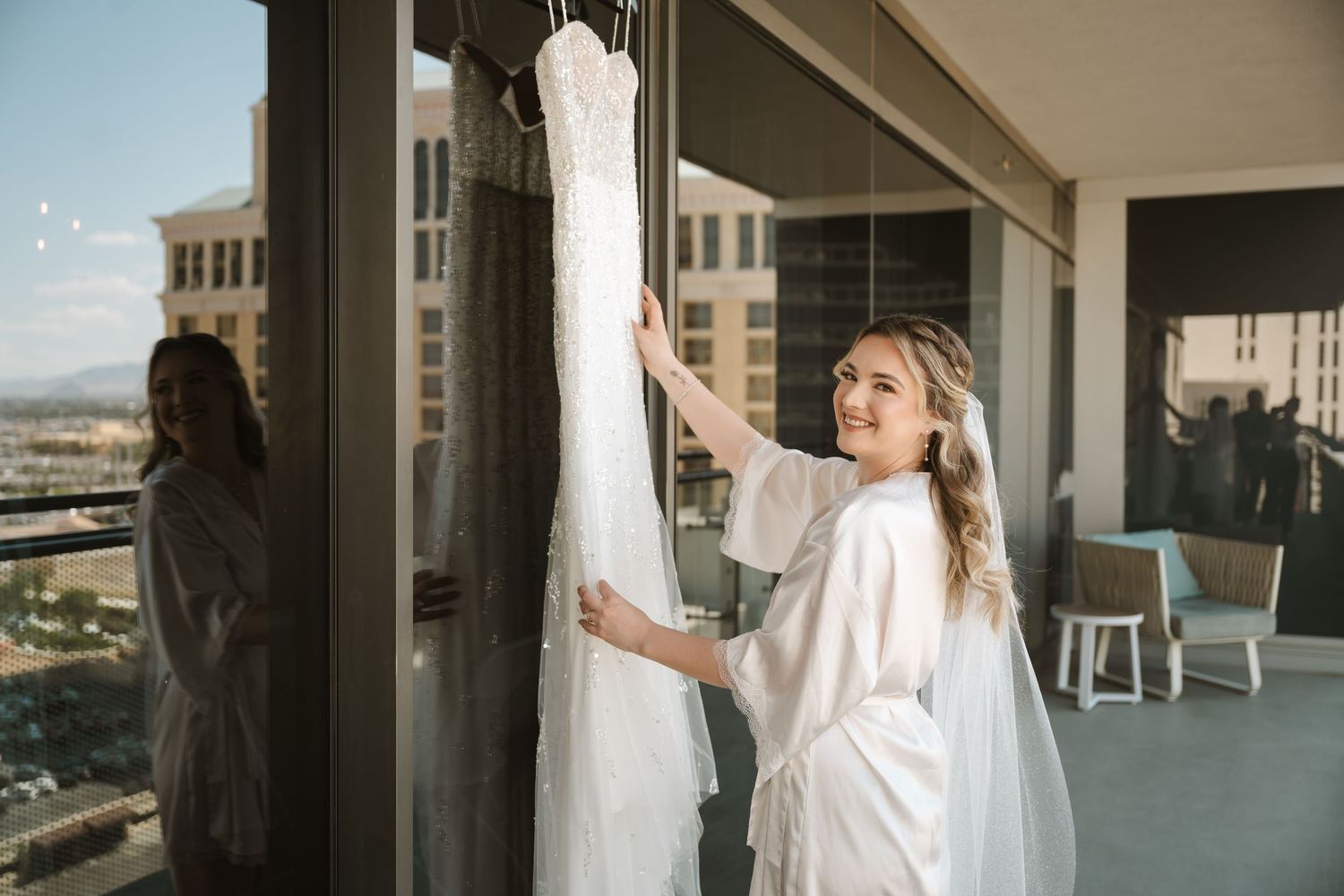 A person in a white robe reaches for a wedding dress hanging on a balcony.