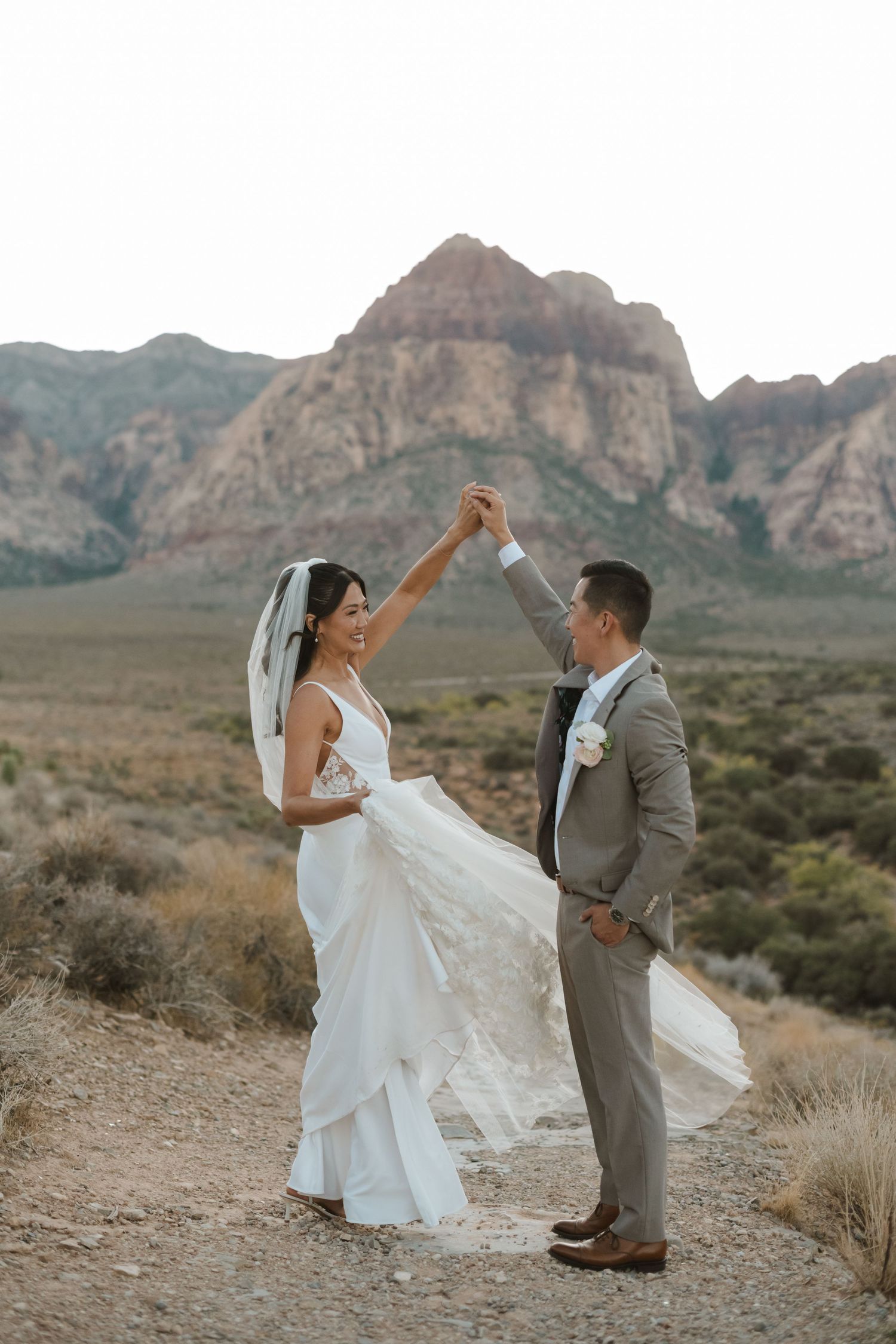 A bride and groom share a romantic dance at Red Rock Canyon, Nevada, with stunning desert mountains in the background.