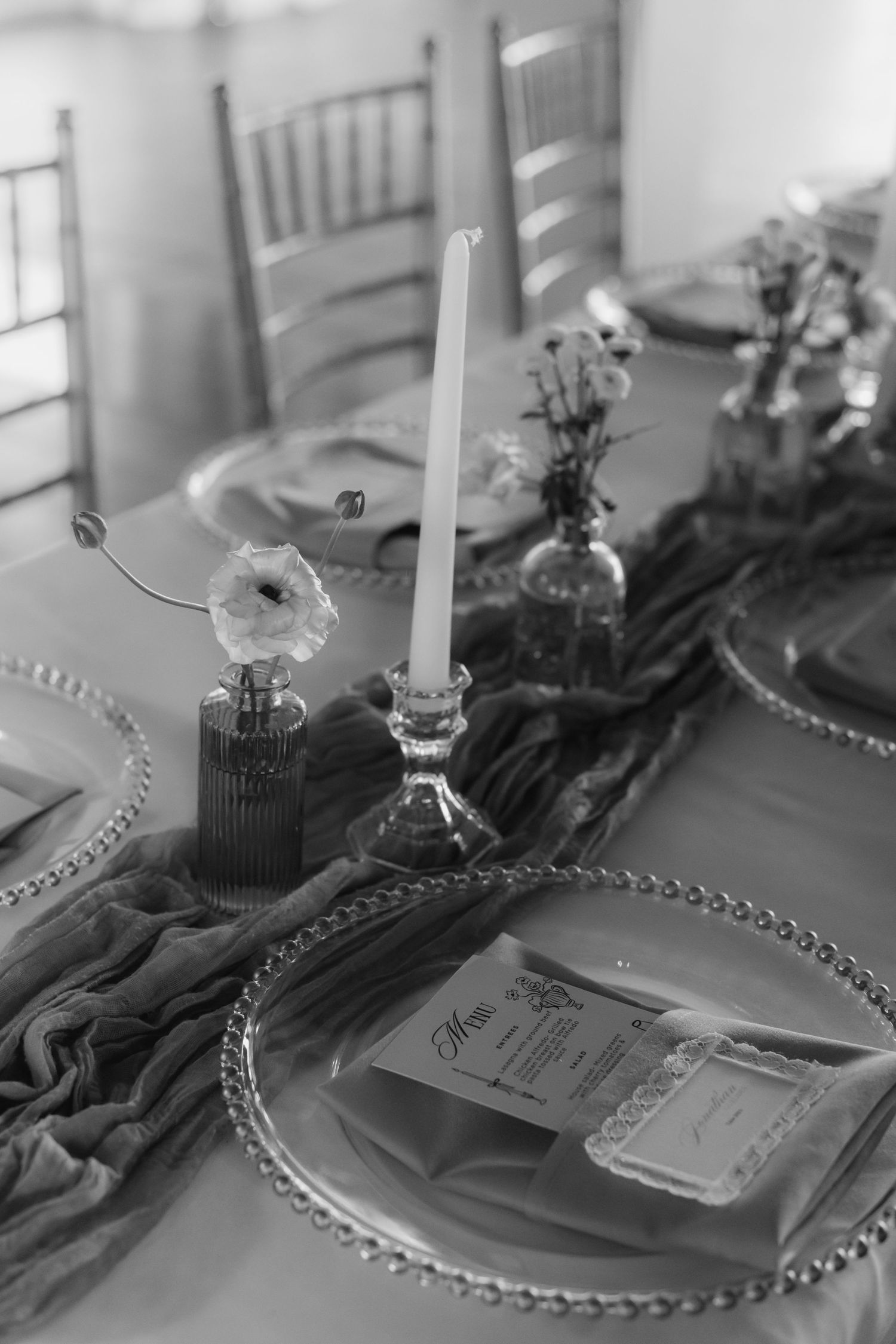 Elegant black and white wedding table setting with candles, floral accents, beaded charger plates, and menu cards.