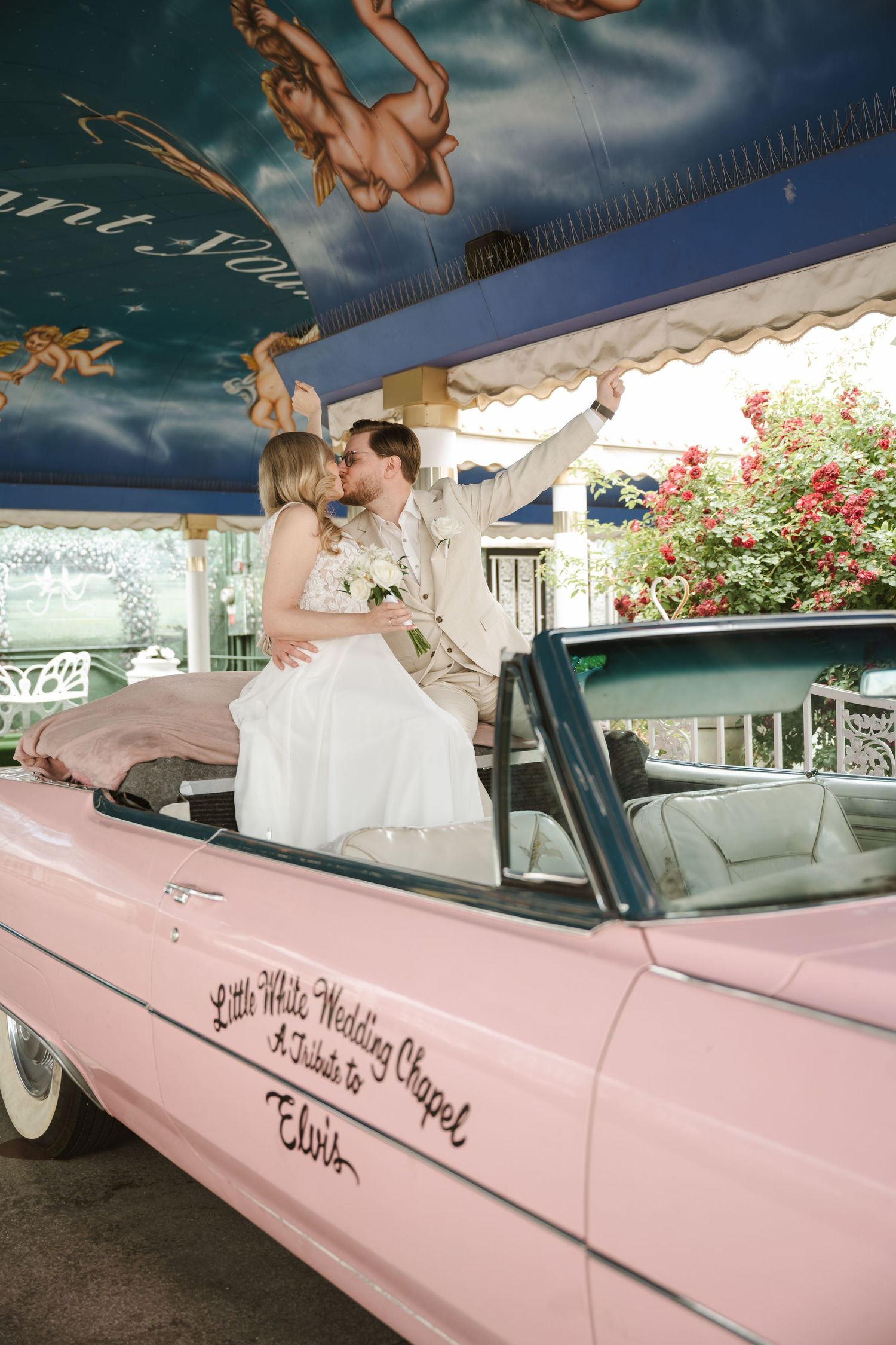 A couple shares a romantic moment in a pink vintage convertible under a decorated ceiling.