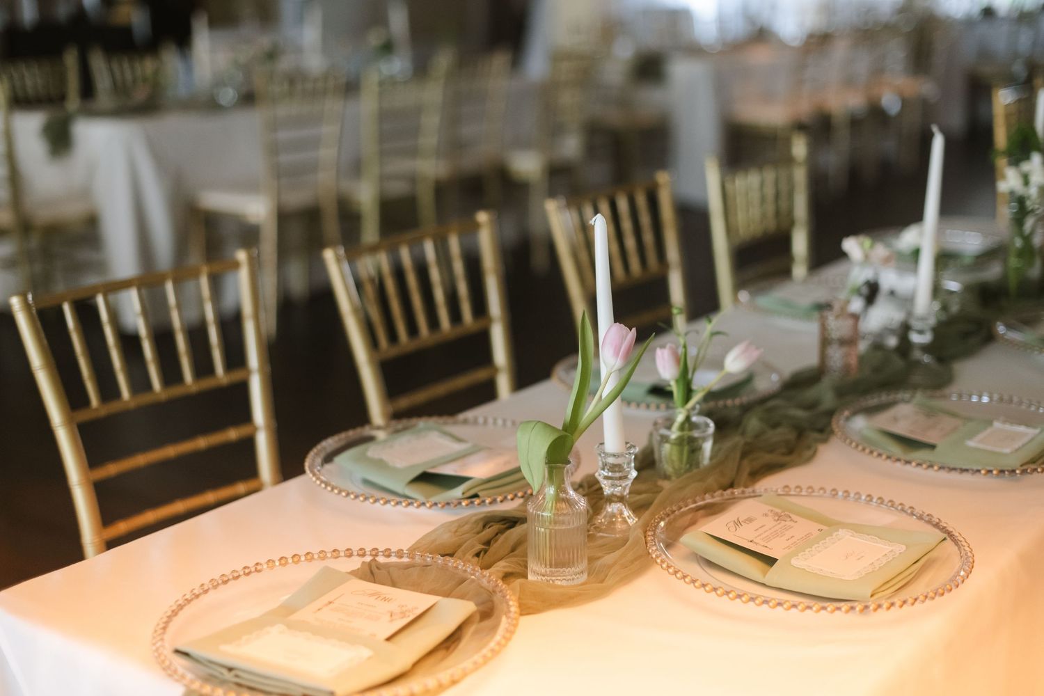 Elegant wedding reception table with gold chiavari chairs, beaded charger plates, taper candles, and fresh tulip centerpieces.