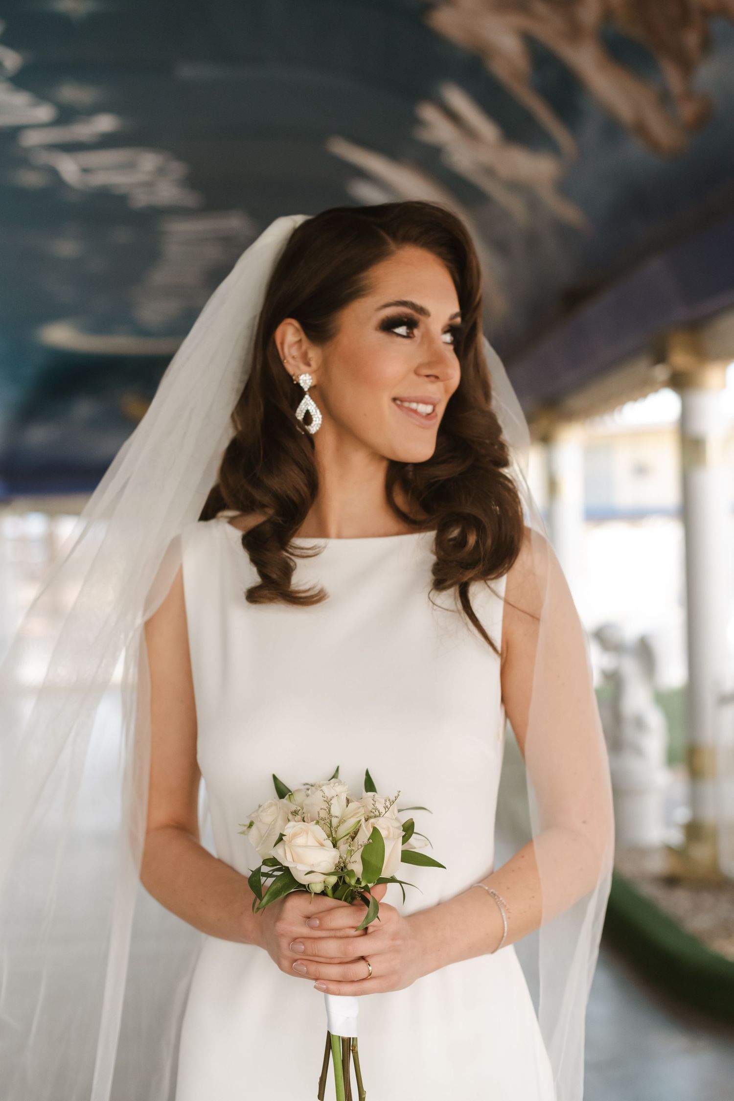 Bride in elegant white dress holding bouquet of white roses during wedding photoshoot.
