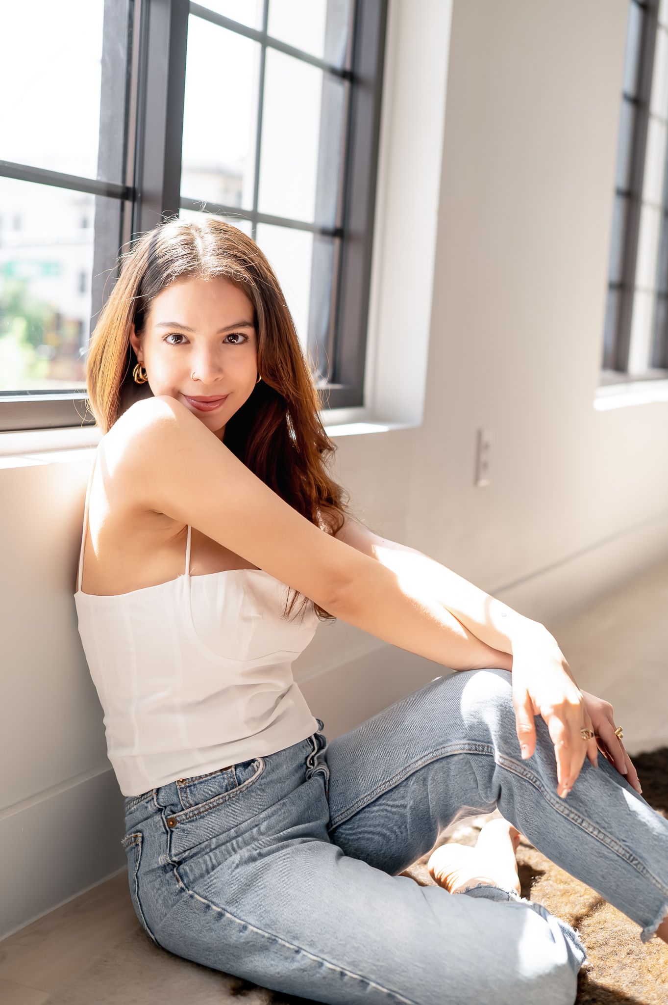 A casual portrait series of someone posing by windows in jeans and a white tank top.