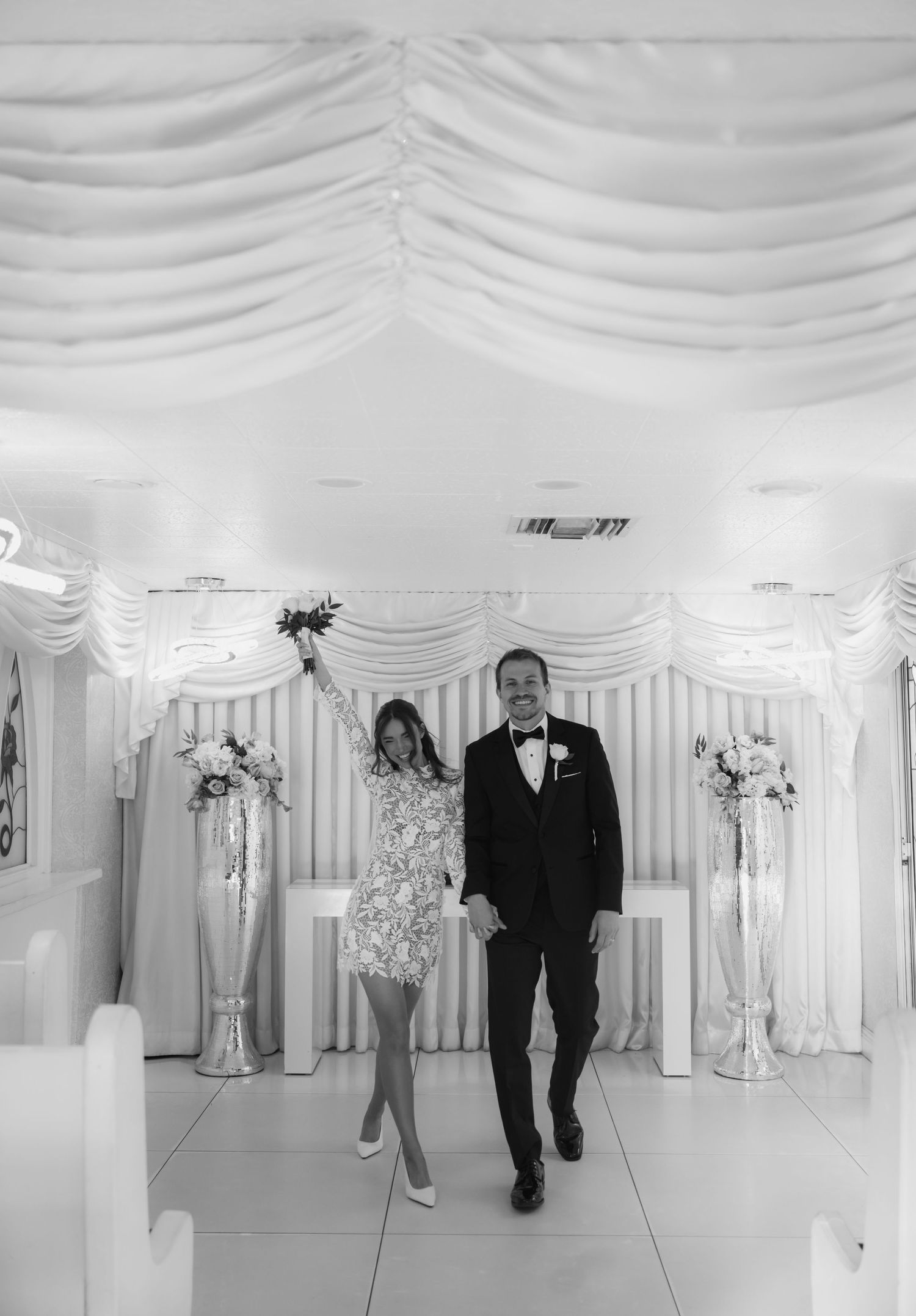 Black and white photo of a newlywed couple walking down the aisle in a decorated wedding chapel.