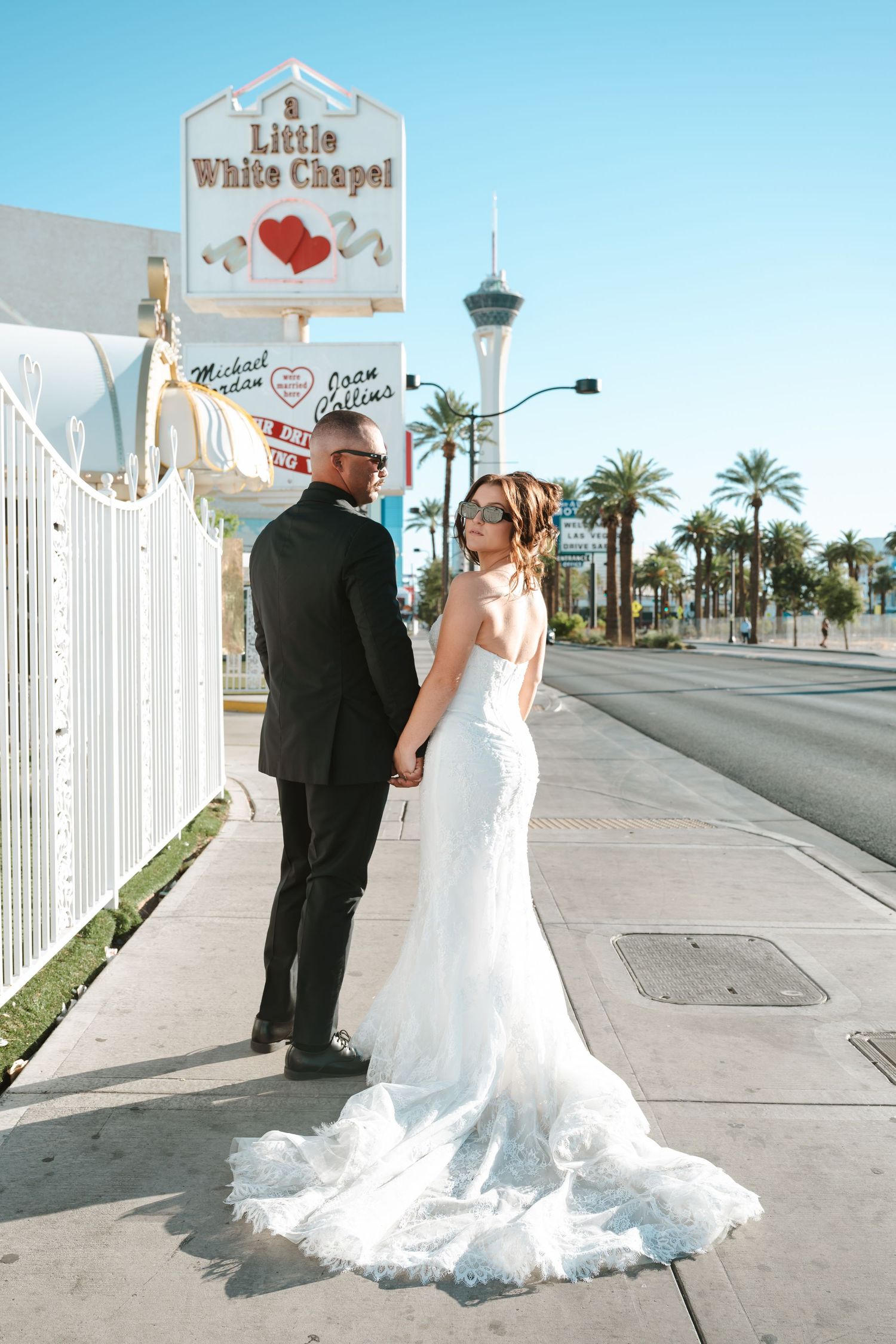 Bride and groom holding hands outside the Little White Chapel in Las Vegas with the Stratosphere tower in the background.