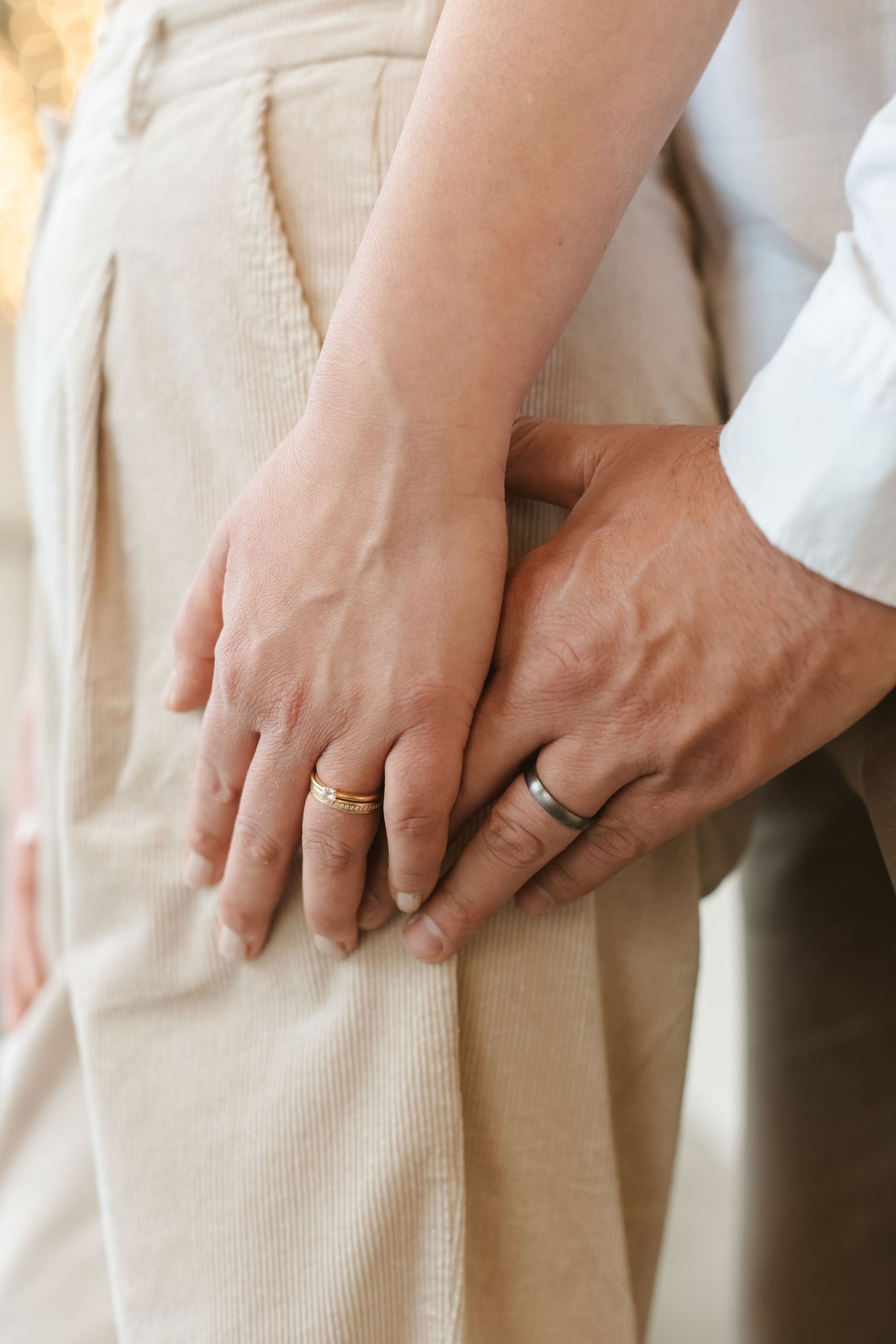 Close-up of hands wearing wedding rings against neutral clothing background.