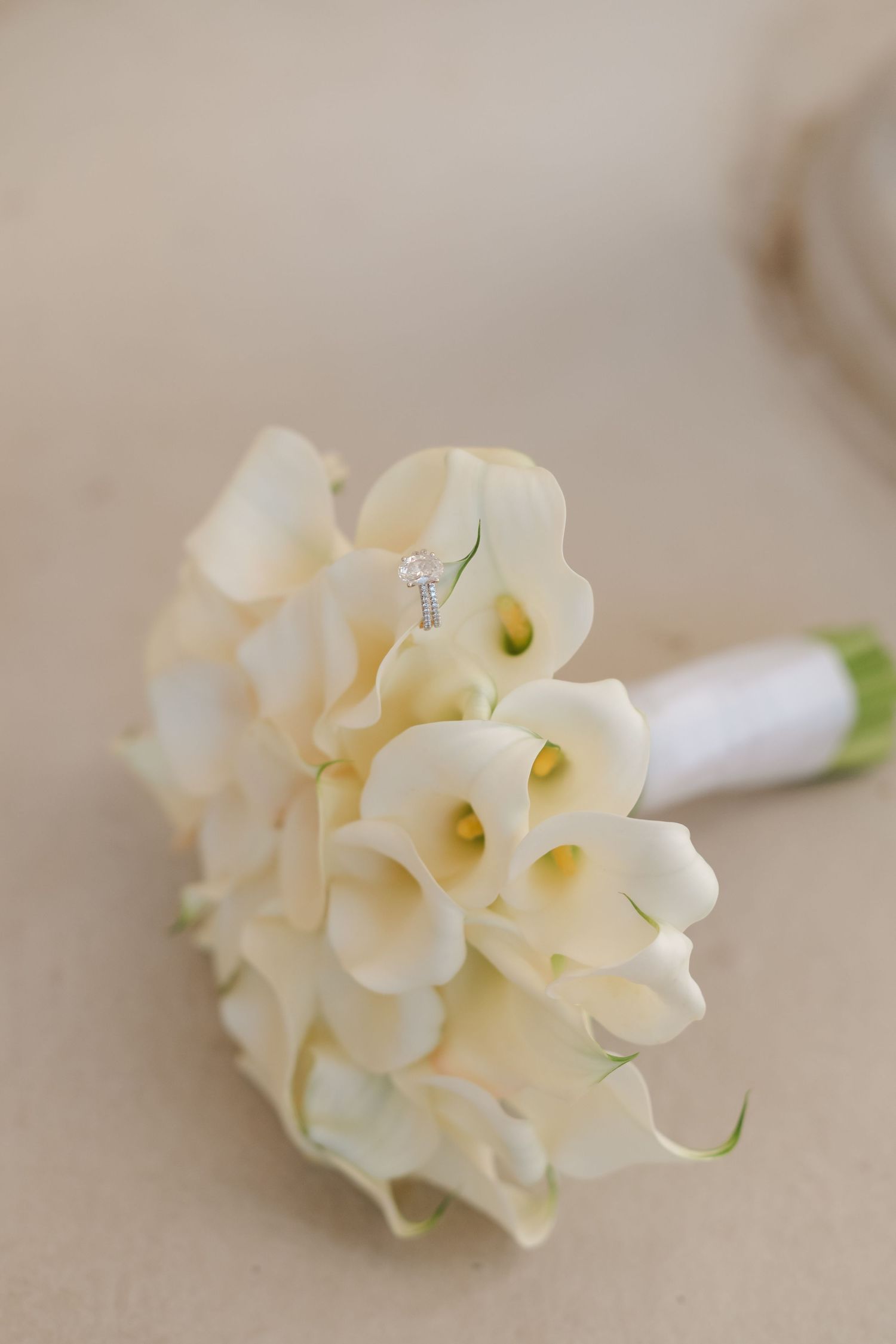 Elegant bridal bouquet of white calla lilies with a diamond engagement ring nestled among the blooms.