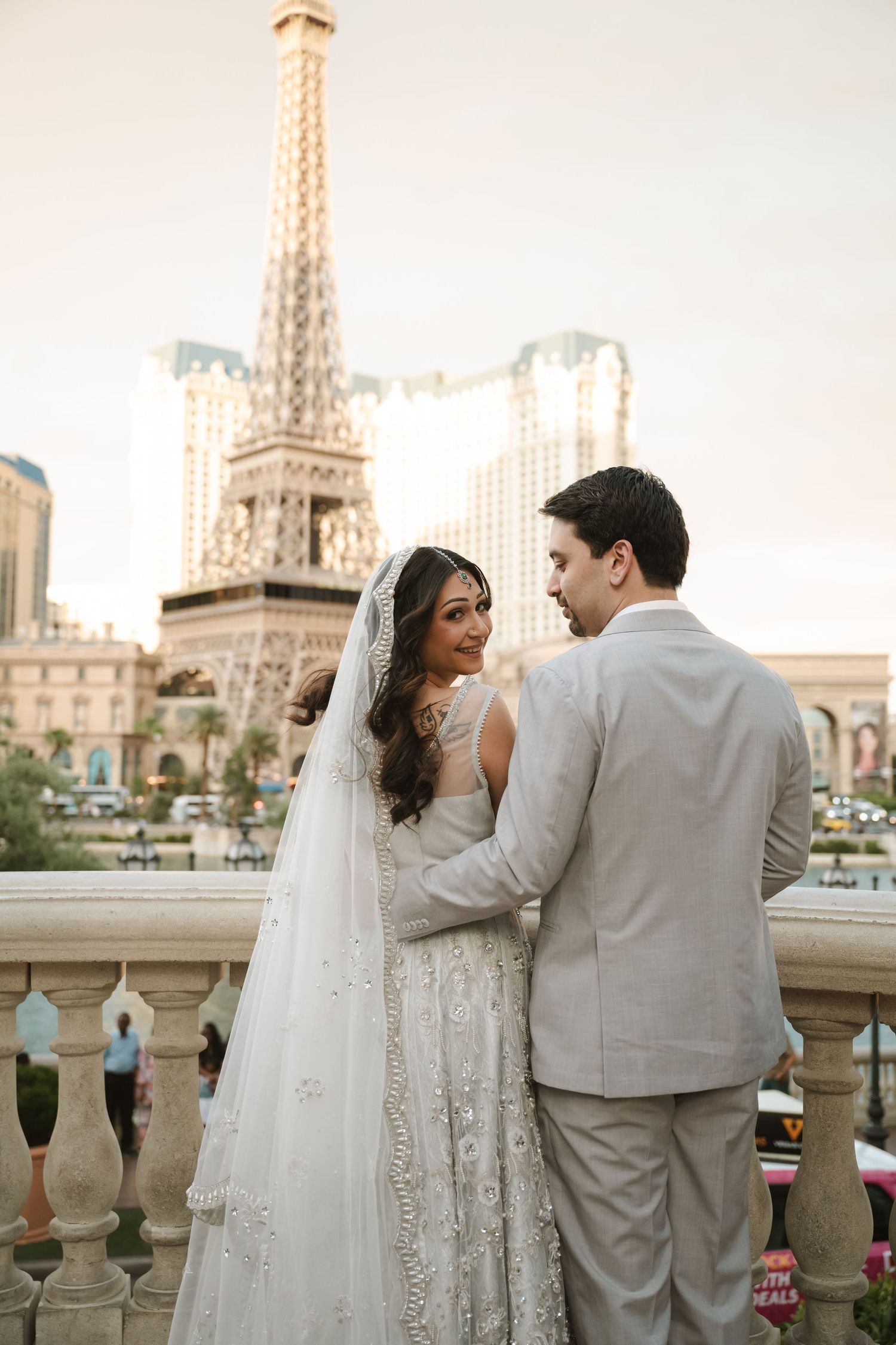 Bride and groom pose romantically on a balcony with the Paris Las Vegas Eiffel Tower replica glowing at sunset.