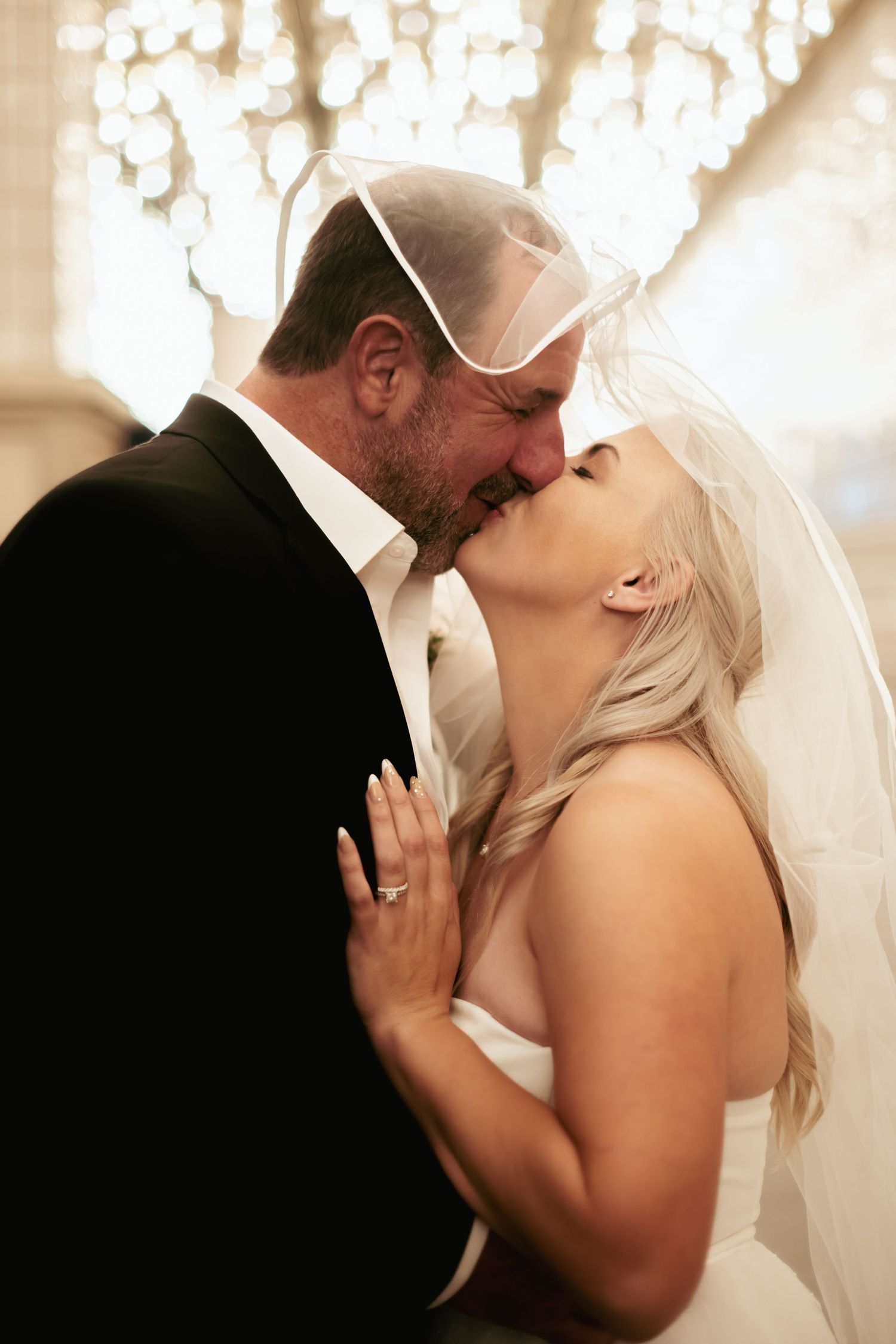 A romantic wedding portrait with bokeh lights as the couple shares an intimate kiss.