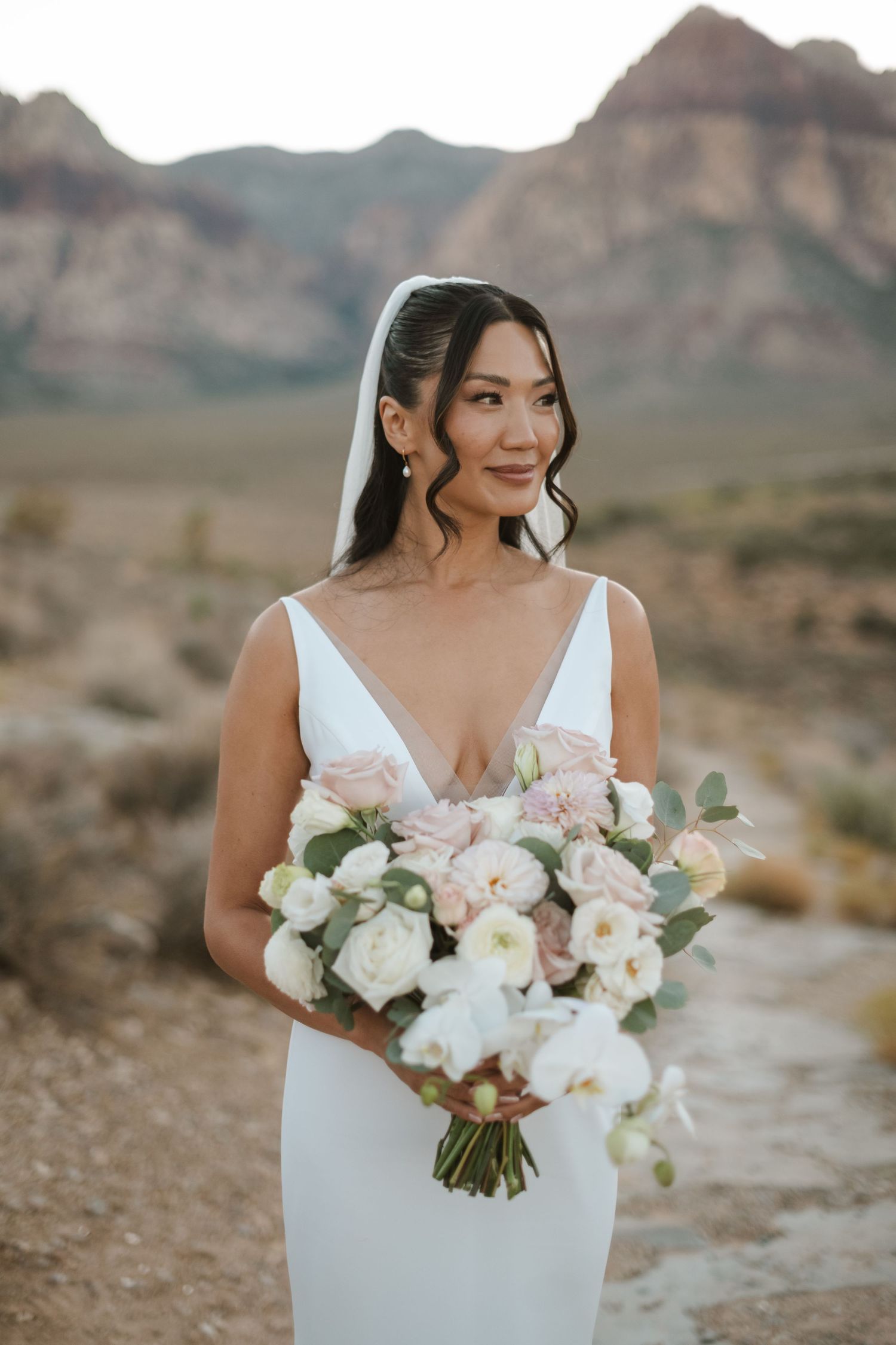Bride in white gown holds blush bouquet at Red Rock Canyon desert wedding backdrop.