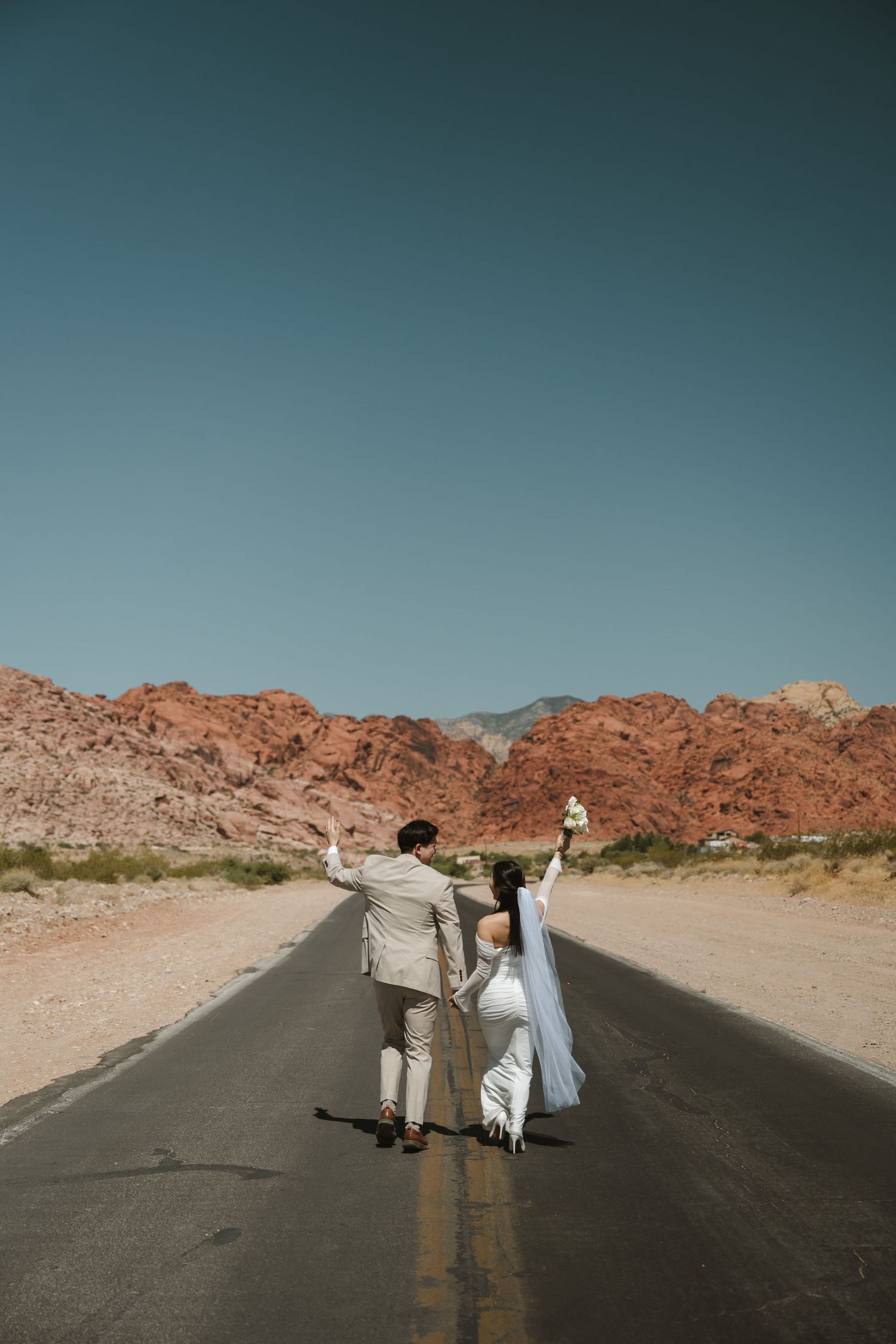 Bride and groom celebrating on a desert road with red rock mountains, Las Vegas elopement photo.