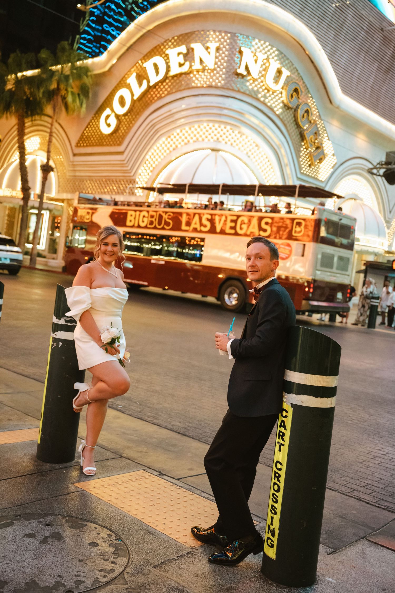 Bride and groom pose outside Golden Nugget casino in Las Vegas at night with Big Bus Tours double-decker in background.