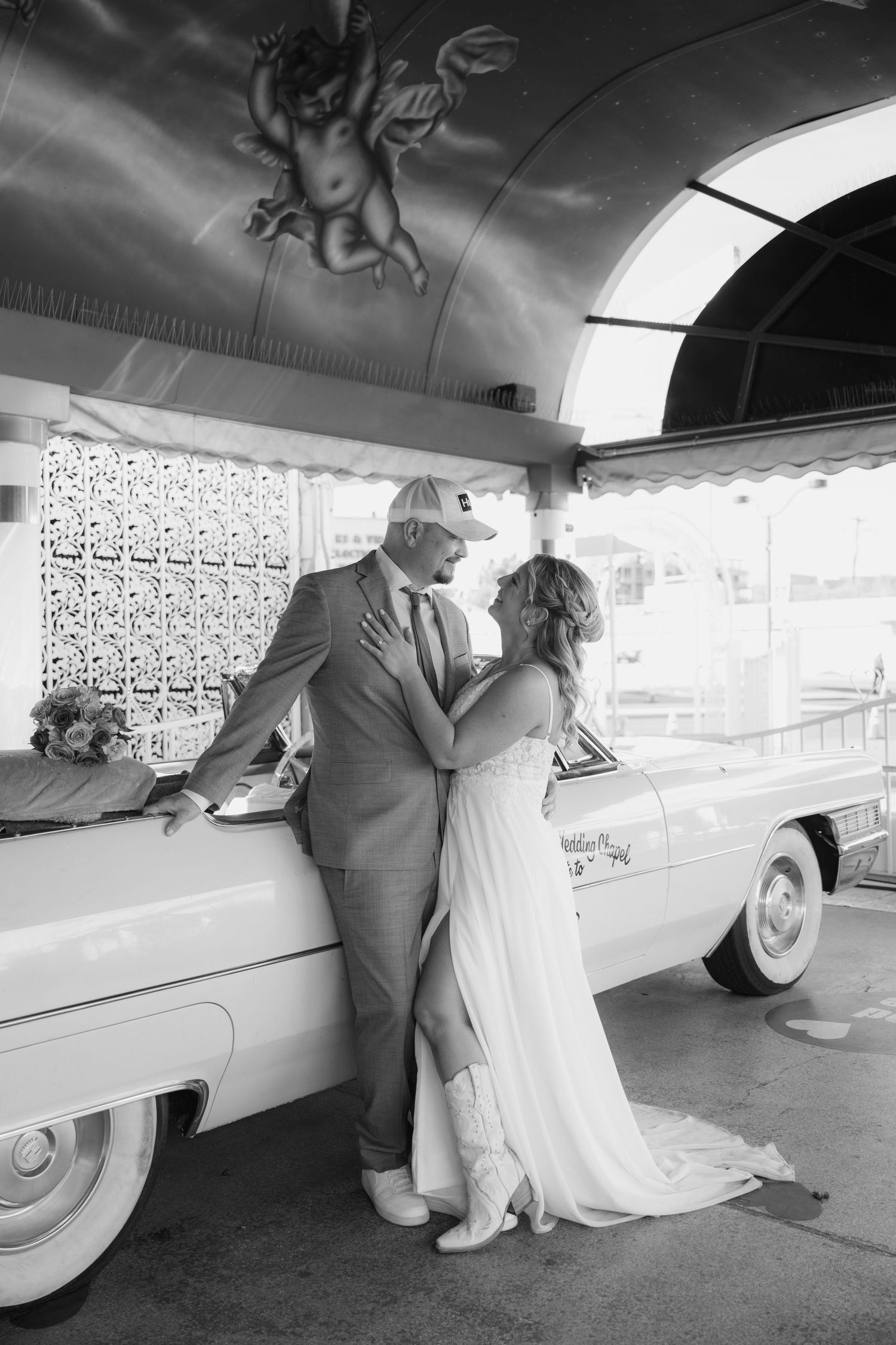 Black and white wedding photos showing a couple near a classic car at a vintage chapel.