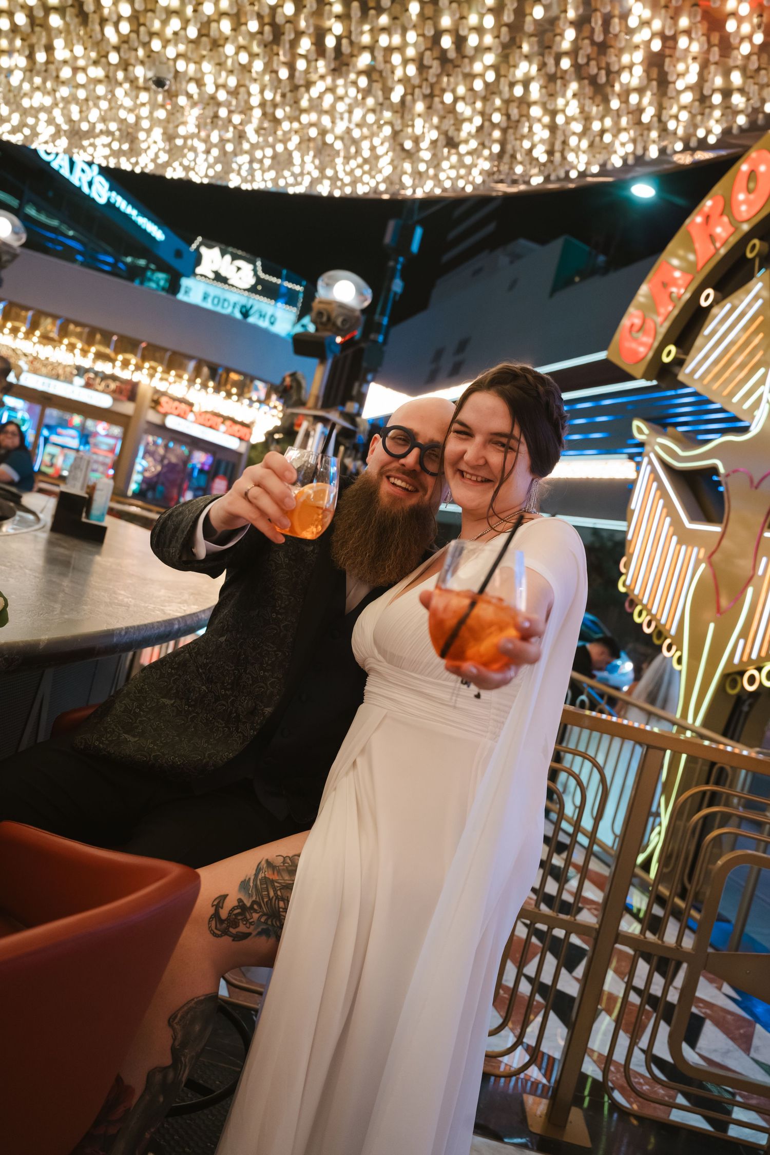 Friends toasting with orange cocktails at a modern bar with glowing lights and decorative lighting.